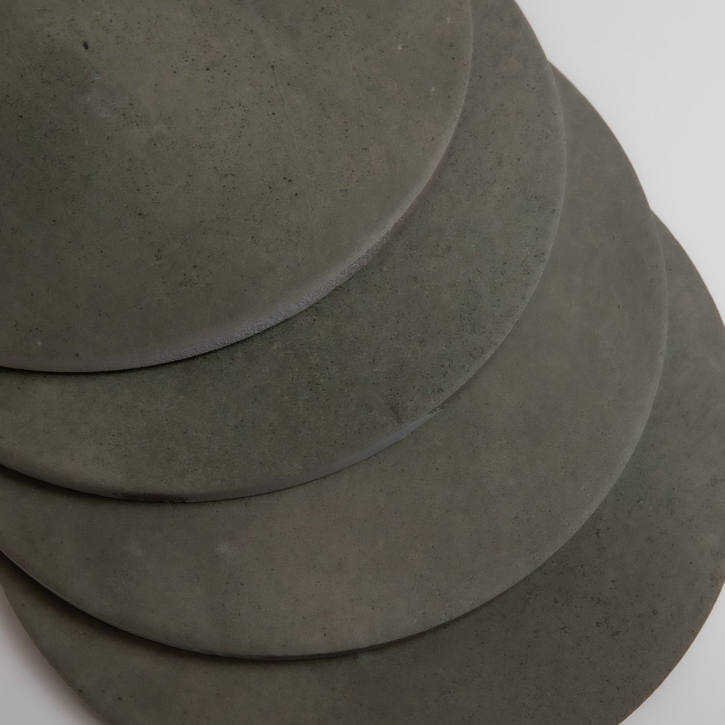 Four overlapping round black Cardon stone samples by Finca, arranged diagonally on a white surface.