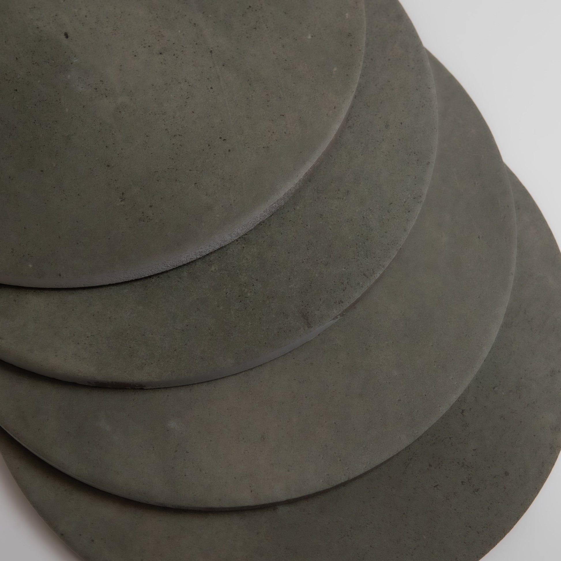 Four overlapping round black Cardon stone samples by Finca, arranged diagonally on a white surface.