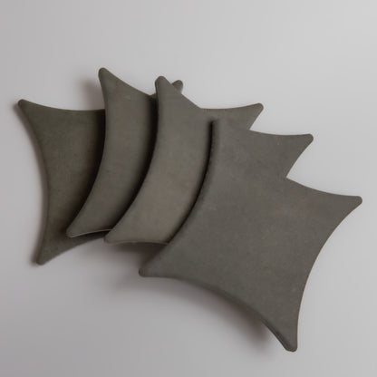 Four gray, square Cardon pillows by Finca are arranged in an overlapping pattern on a plain surface.