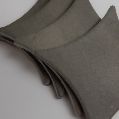 Cardon sample tiles by Finca in curved gray concrete, smooth texture and rounded corners, stacked on a white surface.