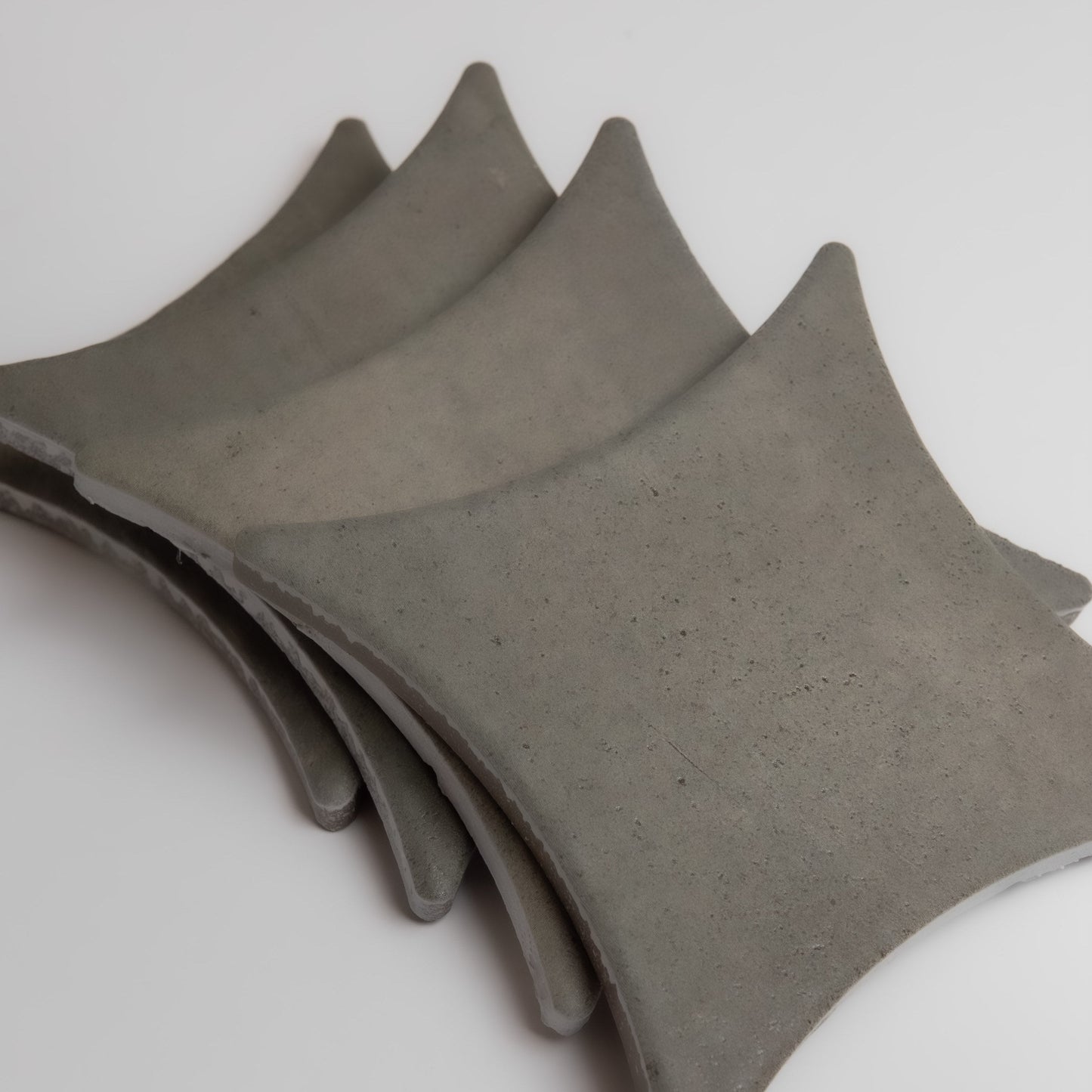 Four curved, gray Cardon concrete tiles by Finca are stacked slightly offset on a white background.