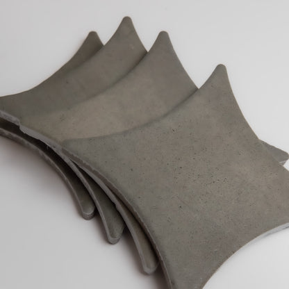 Four curved, gray Cardon concrete tiles by Finca are stacked slightly offset on a white background.