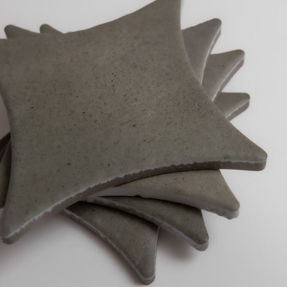Four Cardon sample tiles by Finca, gray diamonds with curved sides and pointed corners, stacked on a white surface.