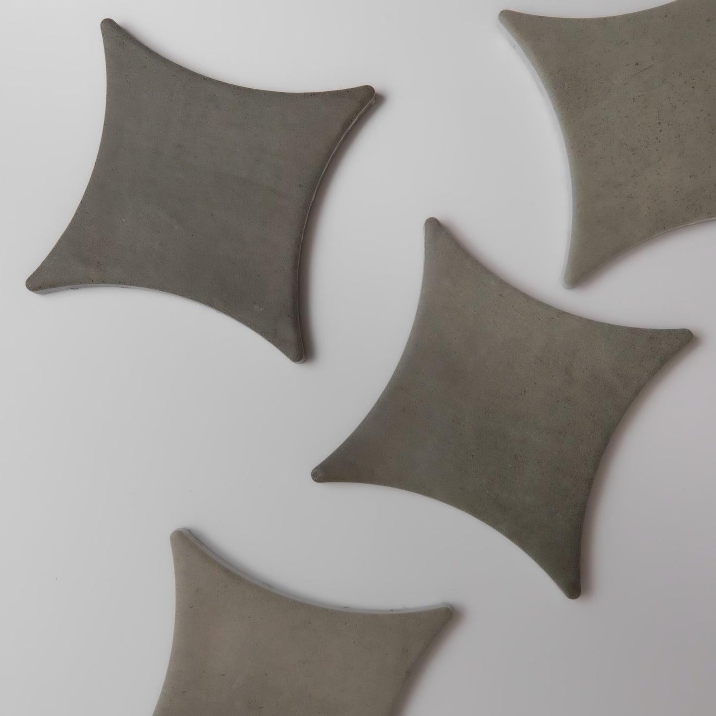 Four gray, star-shaped Cardon ceramic tile samples by Finca are spaced on a white surface in an irregular pattern.