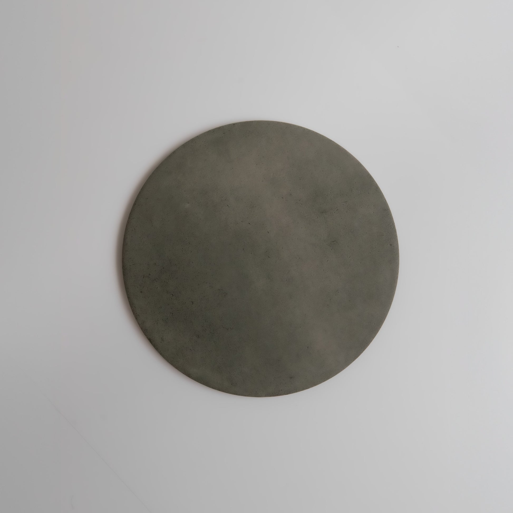 The Finca Cardon sample, a flat round gray stone, displayed on a plain white background.