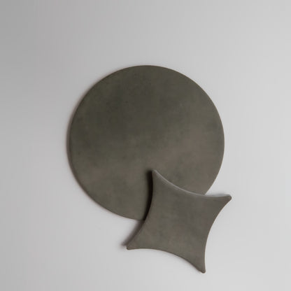 Finca Cardon Sample: minimalist grey ceramic plates, one round and one square, on a plain white background.