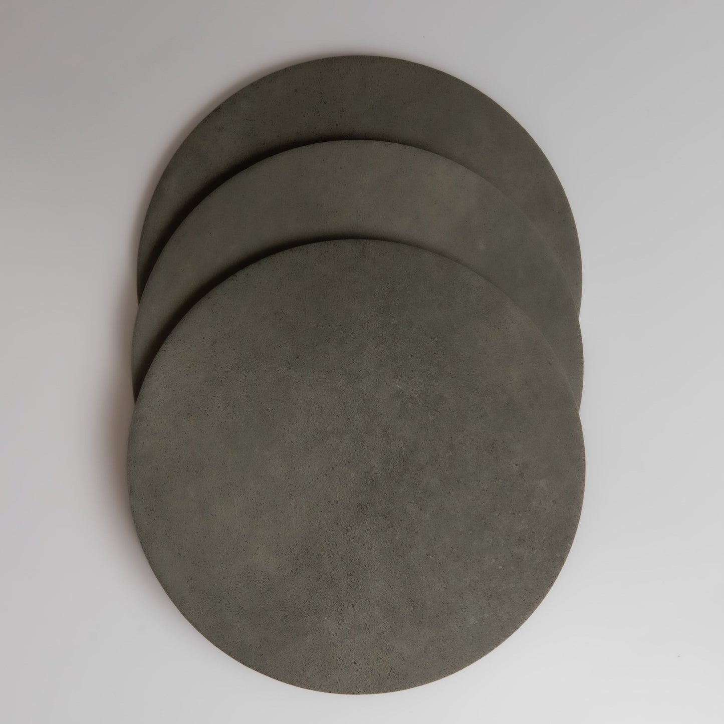Three overlapping round gray Cardon concrete samples by Finca on a white background, viewed from above.