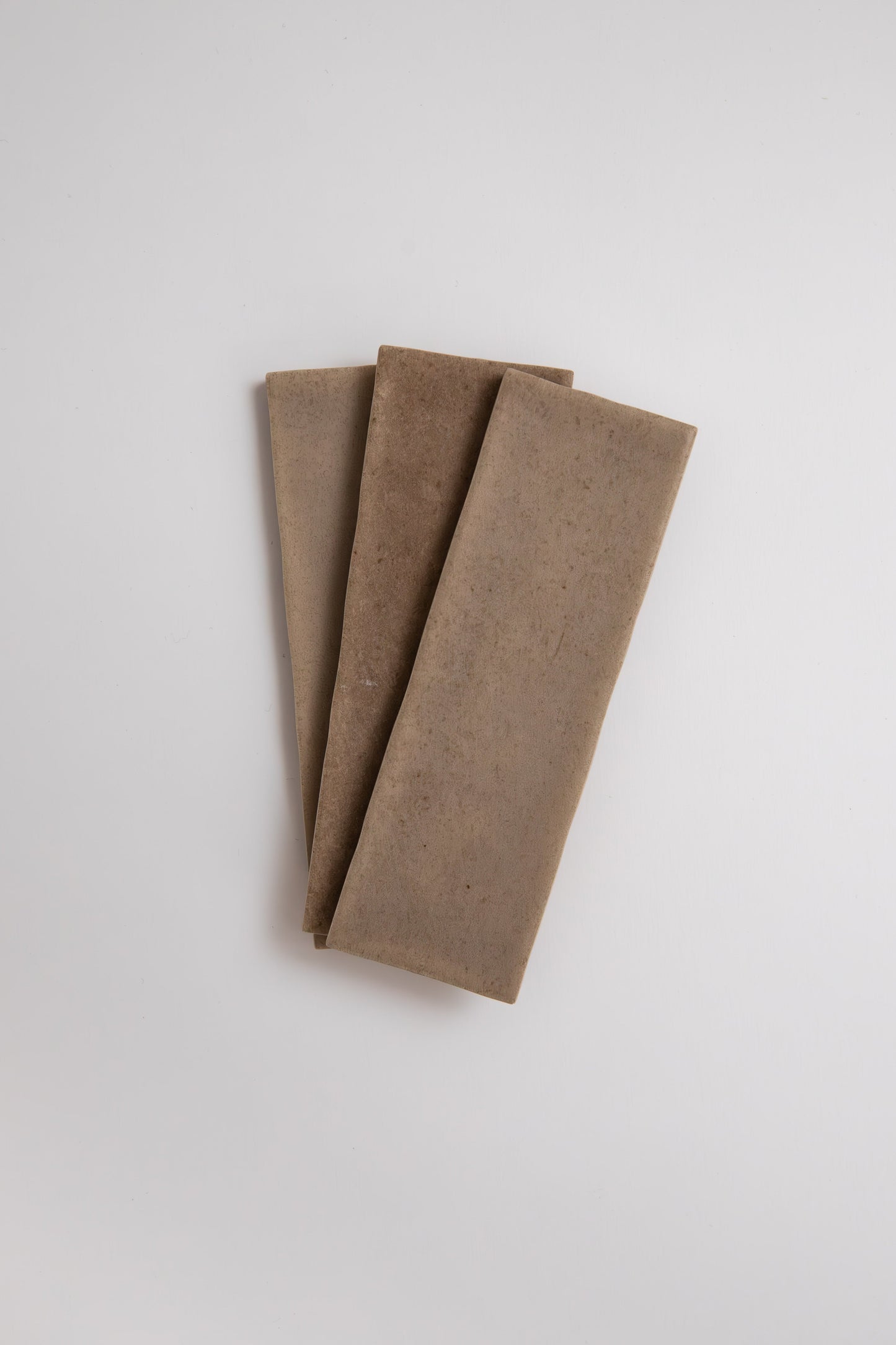 Three Castlegate Brown tiles by Cottage Ivy are arranged in a fan shape on a plain white background.