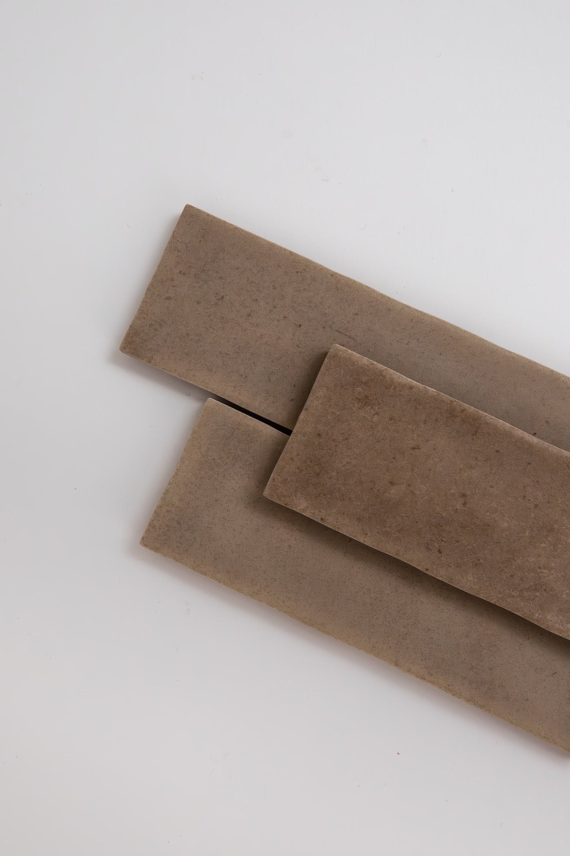 Three Castlegate Brown rectangular tiles by Cottage Ivy overlap diagonally on a plain white background.