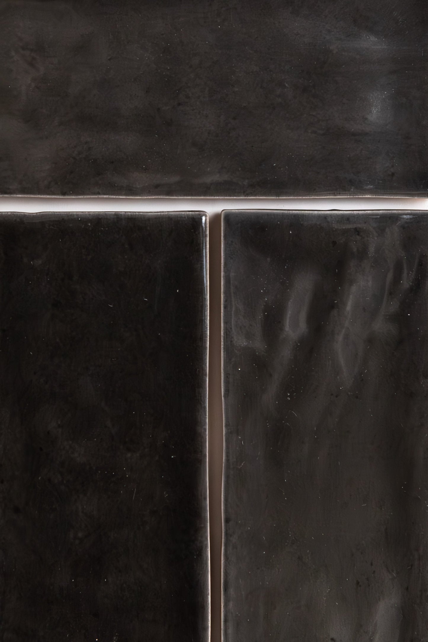 Close-up of three Cobbled Graphite tiles by Cottage Ivy, glossy black with grout lines in a T-shape.