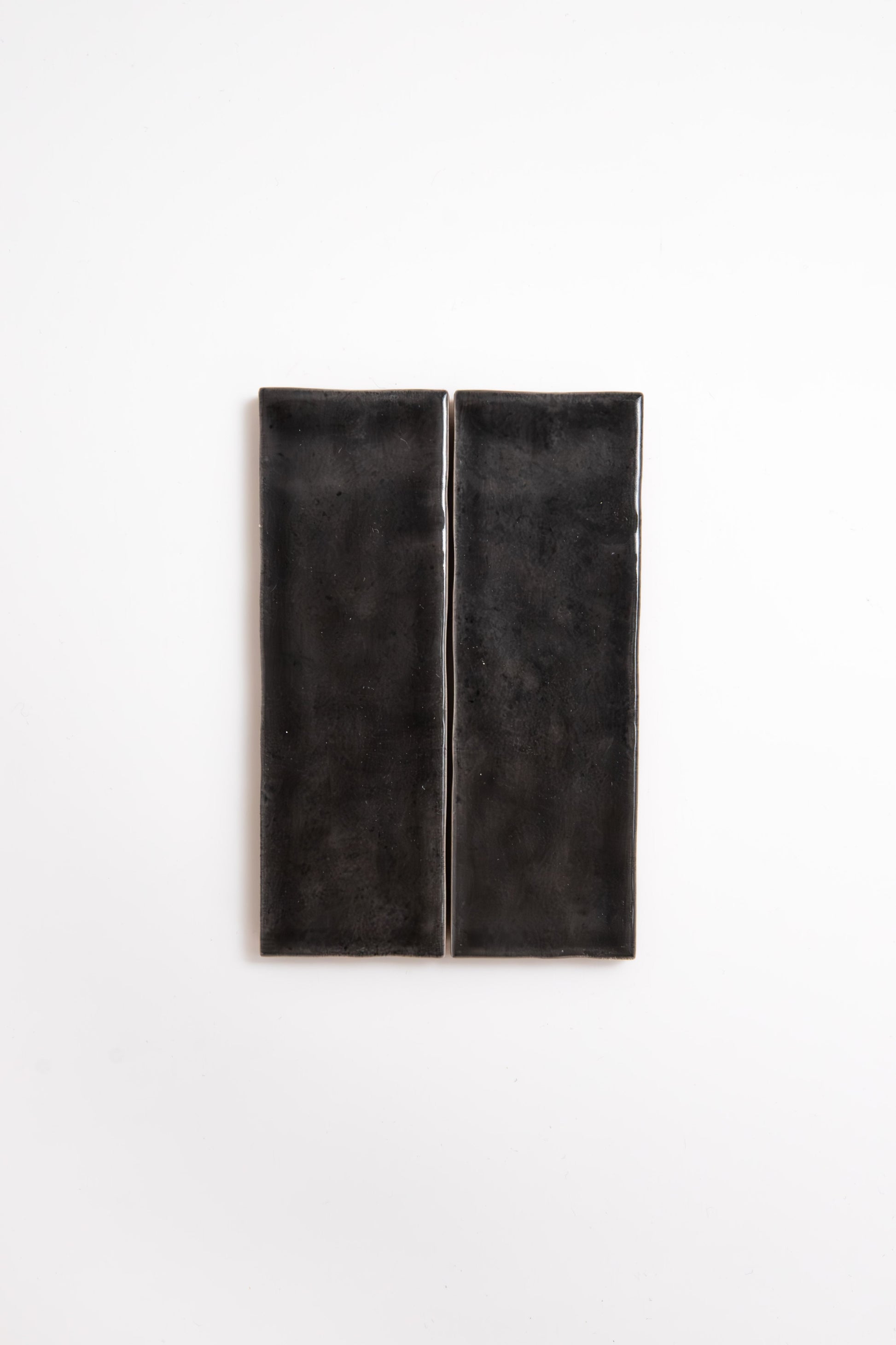 Two Cobbled Graphite tiles by Cottage Ivy, rectangular and glossy black, side by side on a white background.
