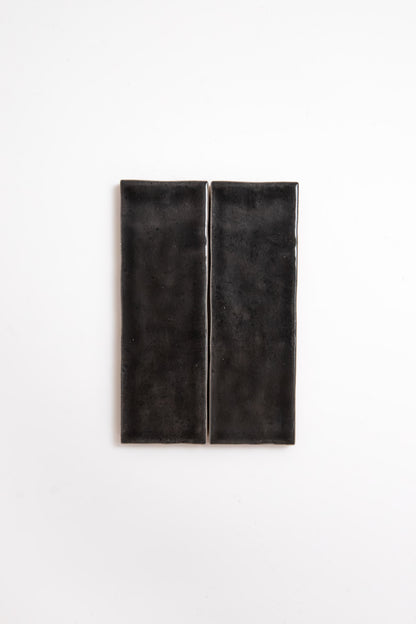 Two Cobbled Graphite tiles by Cottage Ivy, rectangular and glossy black, side by side on a white background.