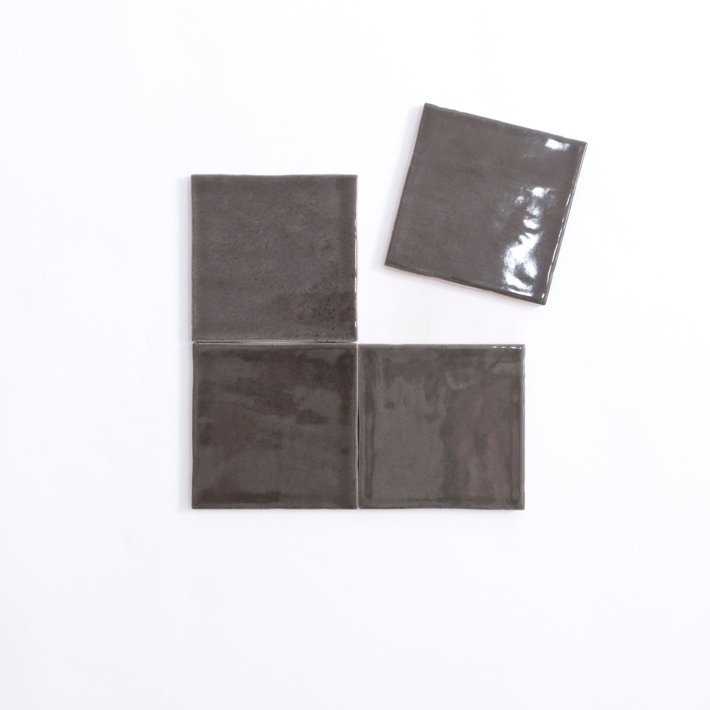Four glossy, square Cobbled Graphite tiles by Cottage Ivy on white; three aligned, one set slightly apart above.
