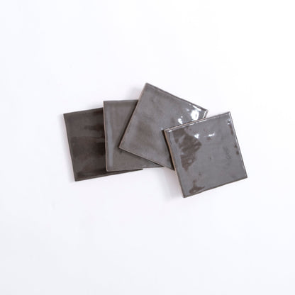 Four glossy Cobbled Graphite tiles by Cottage Ivy overlap on a white background.