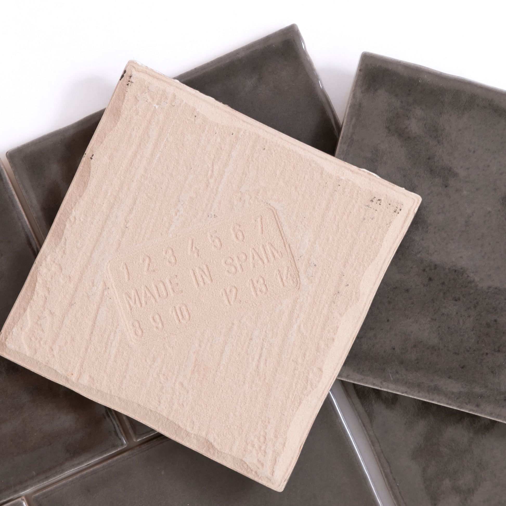 A Cobbled Graphite tile by Cottage Ivy rests atop several glossy dark gray tiles.