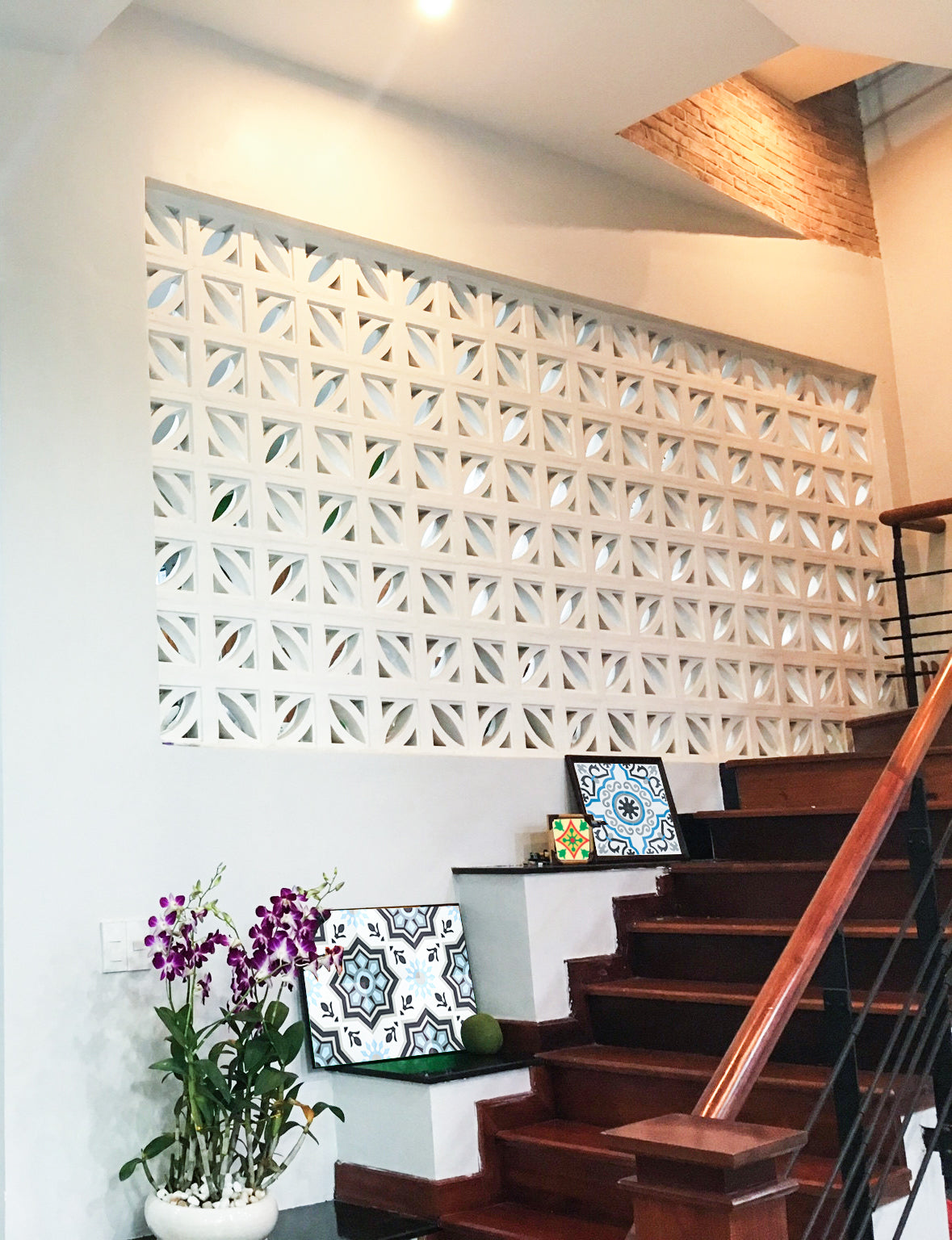 New York Cement Tile's Coz breeze blocks create a decorative wall by a staircase with patterned cushions and a purple orchid.