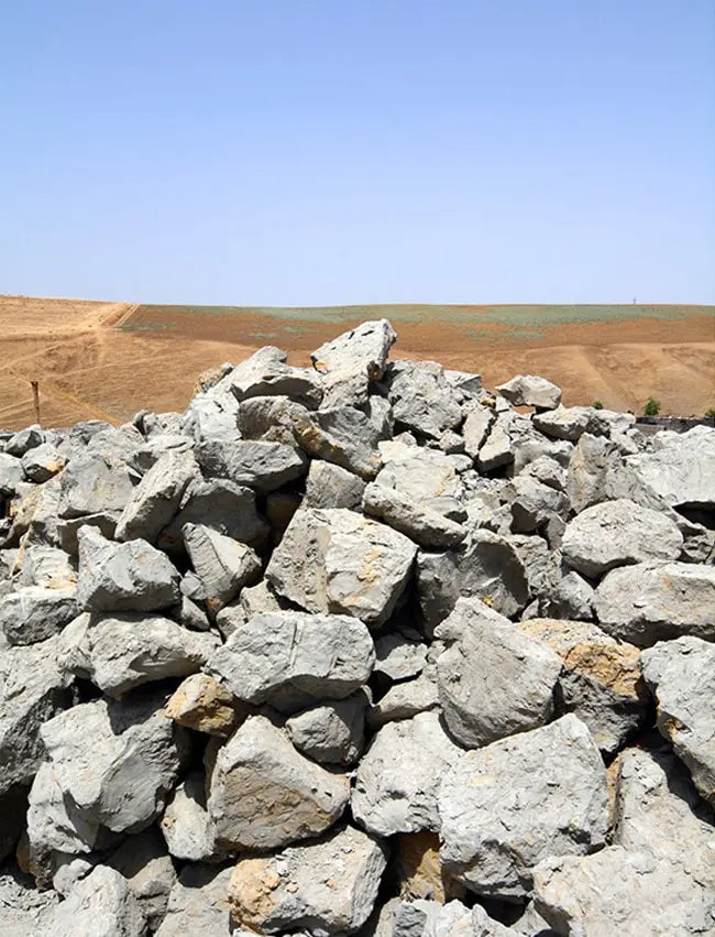A pile of large gray rocks in the foreground with a dry, barren landscape and clear blue sky in the background.