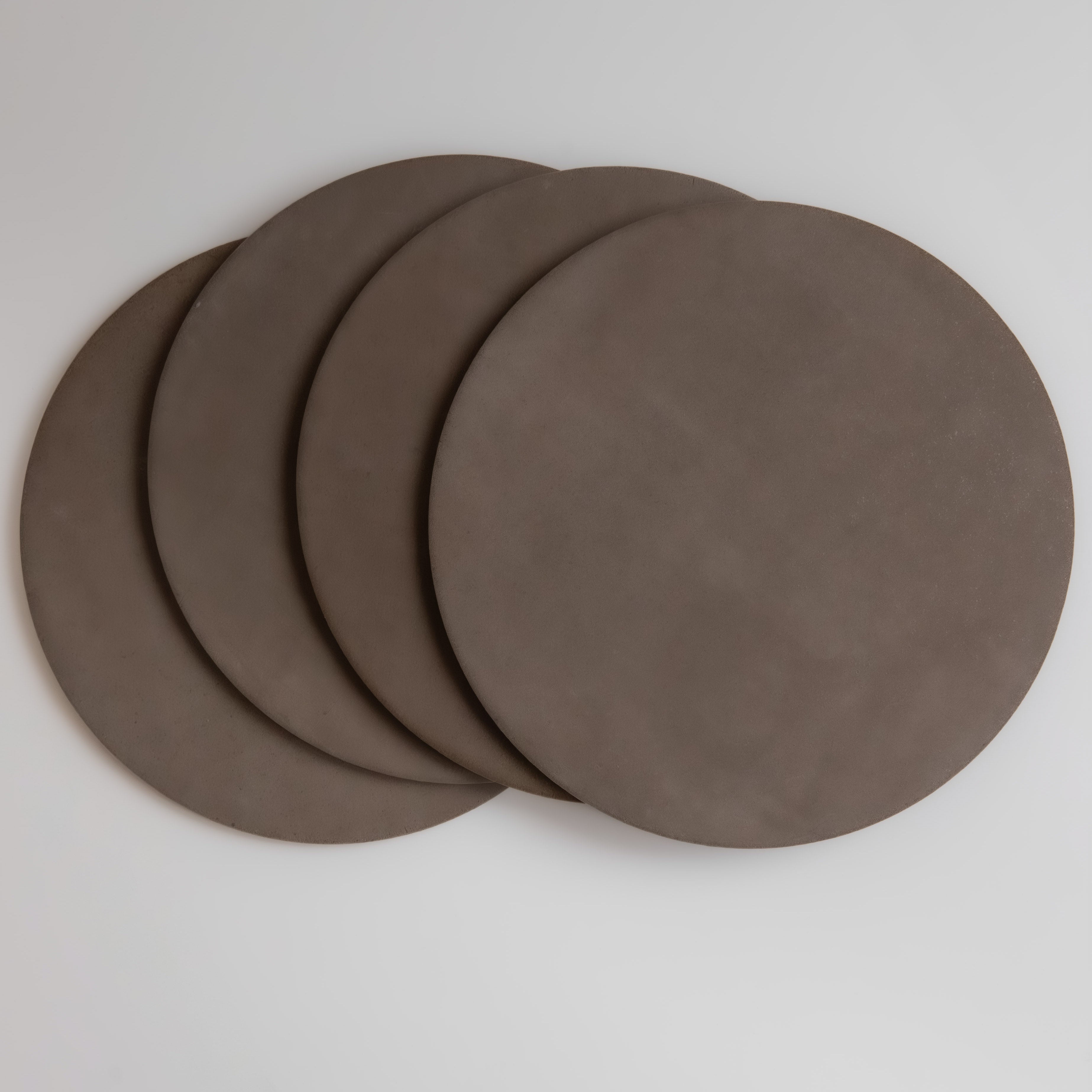 Four round brown coasters on a light gray background