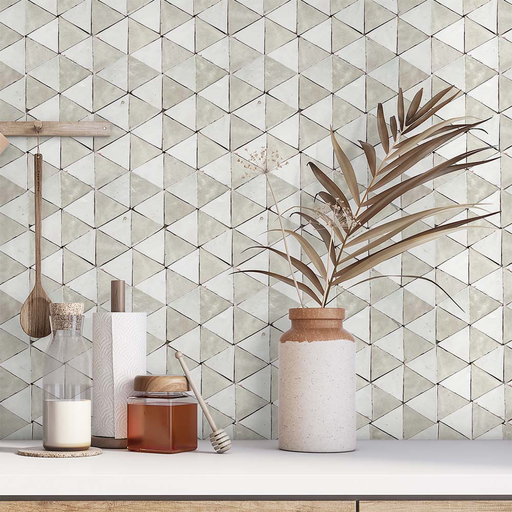 Kitchen counter with jars, utensils, paper towels, and a vase with dried plants set against a geometric tiled backsplash.