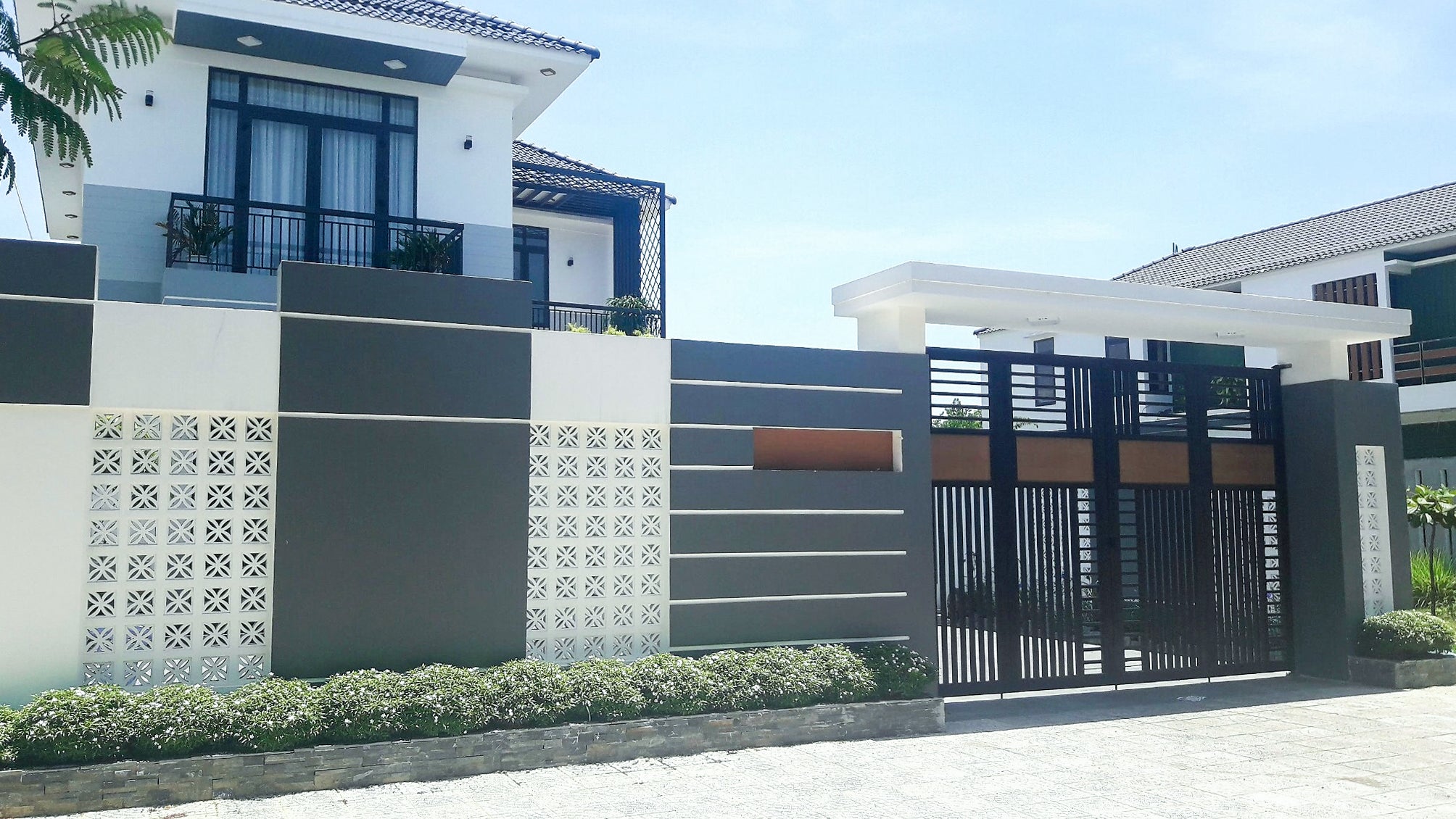 Beeza Sample by New York Cement Tile: geometric gray & white two-story house with black metal gate on a sunny day.