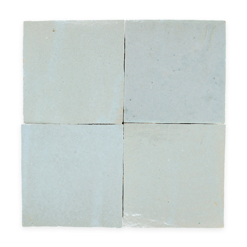 Four light blue, square ceramic tiles arranged in a 2x2 grid with slightly uneven edges and glossy surfaces.