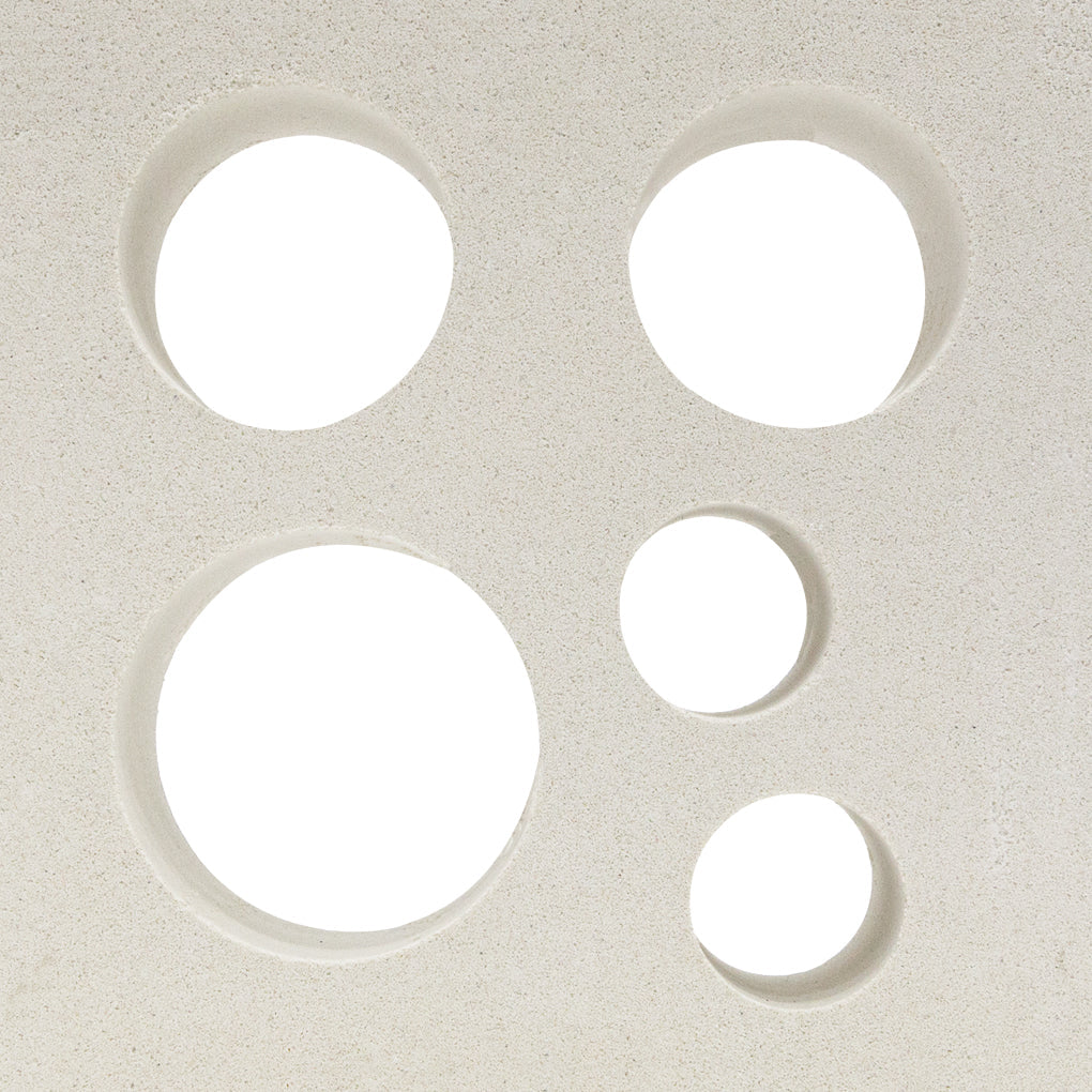 Five circular holes of varying sizes in Jamaica - NBB-015 by New York Cement Tile are arranged on an off-white surface.