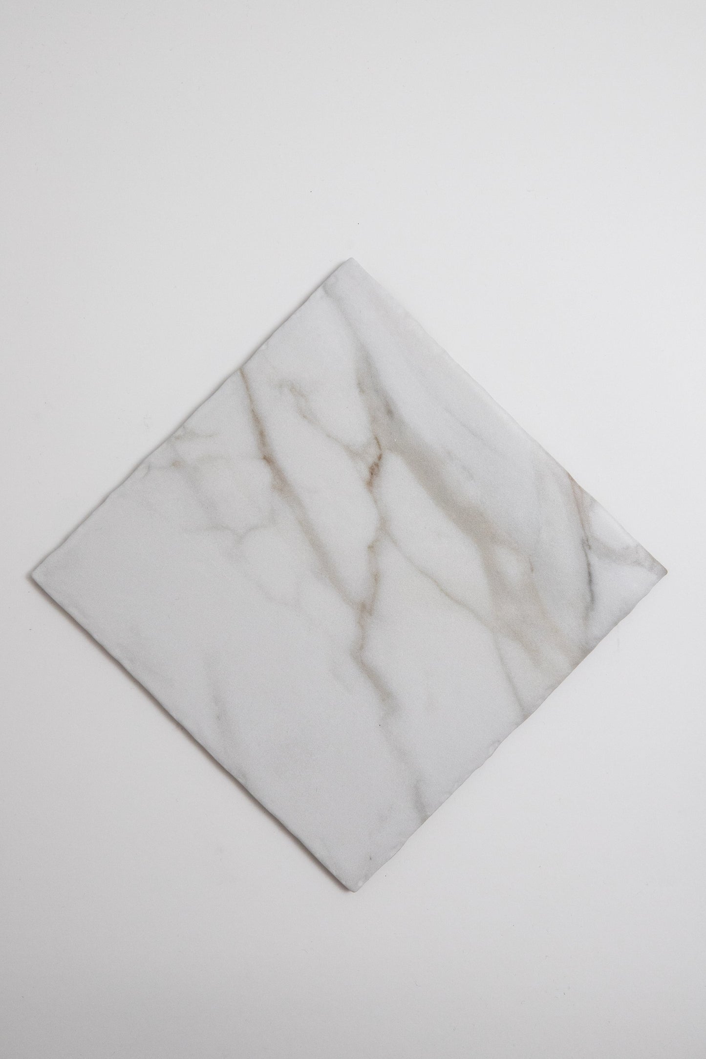 The Tosca Macchia Vecchia sample is a square white marble tile with light gray and brown veining, shown diagonally.