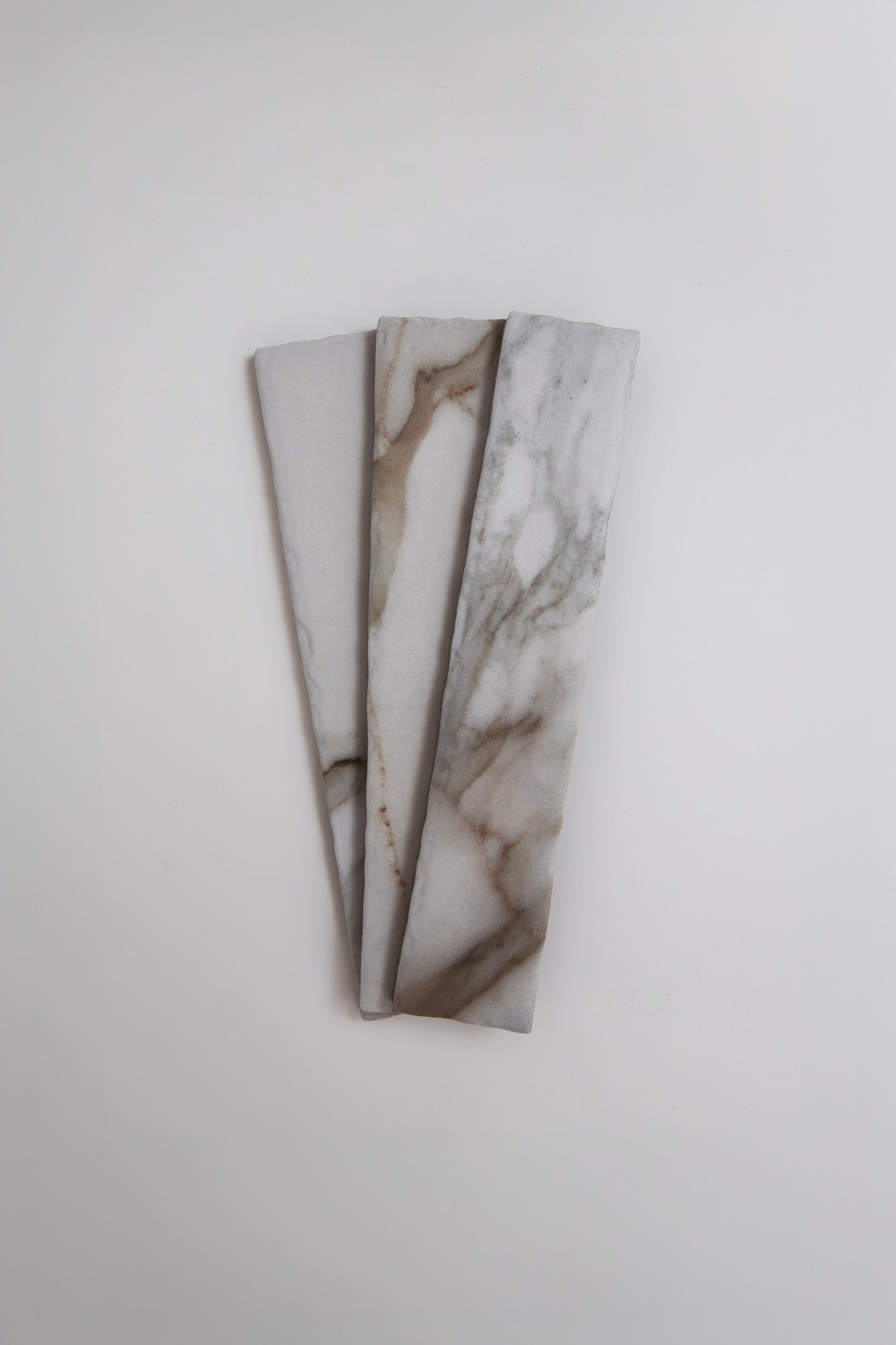 Three Tosca Macchia Vecchia samples with gray and brown veining are fanned out on a white background.