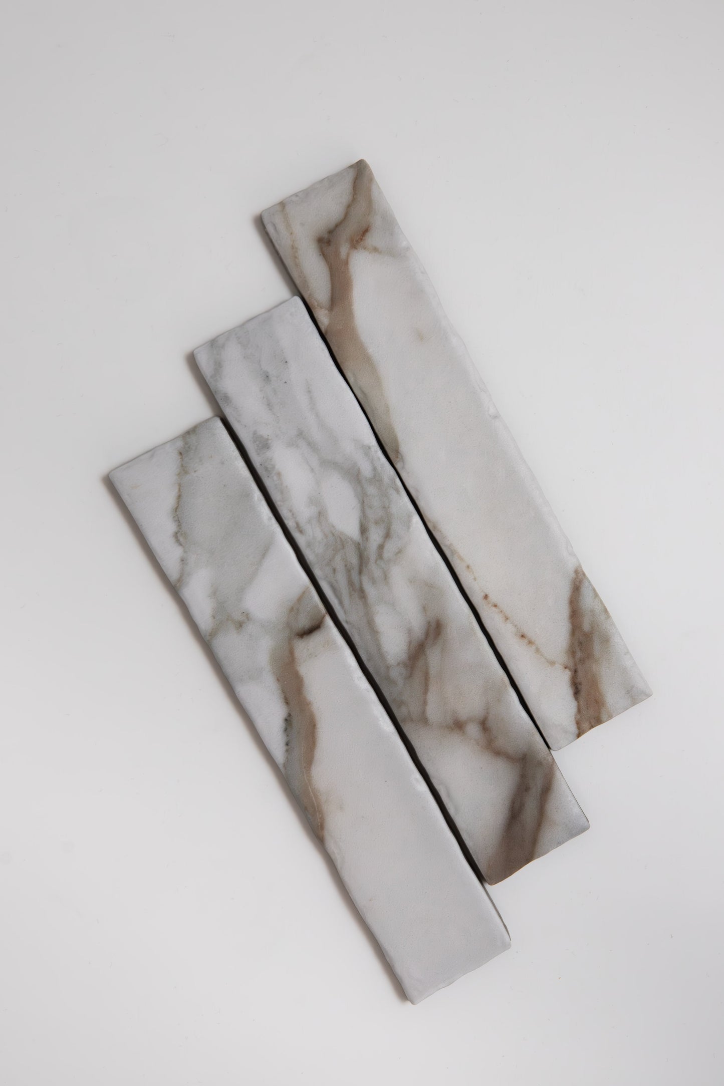 Three Macchia Vecchia marble samples from Tosca, with gray and brown veining, set diagonally on a white background.