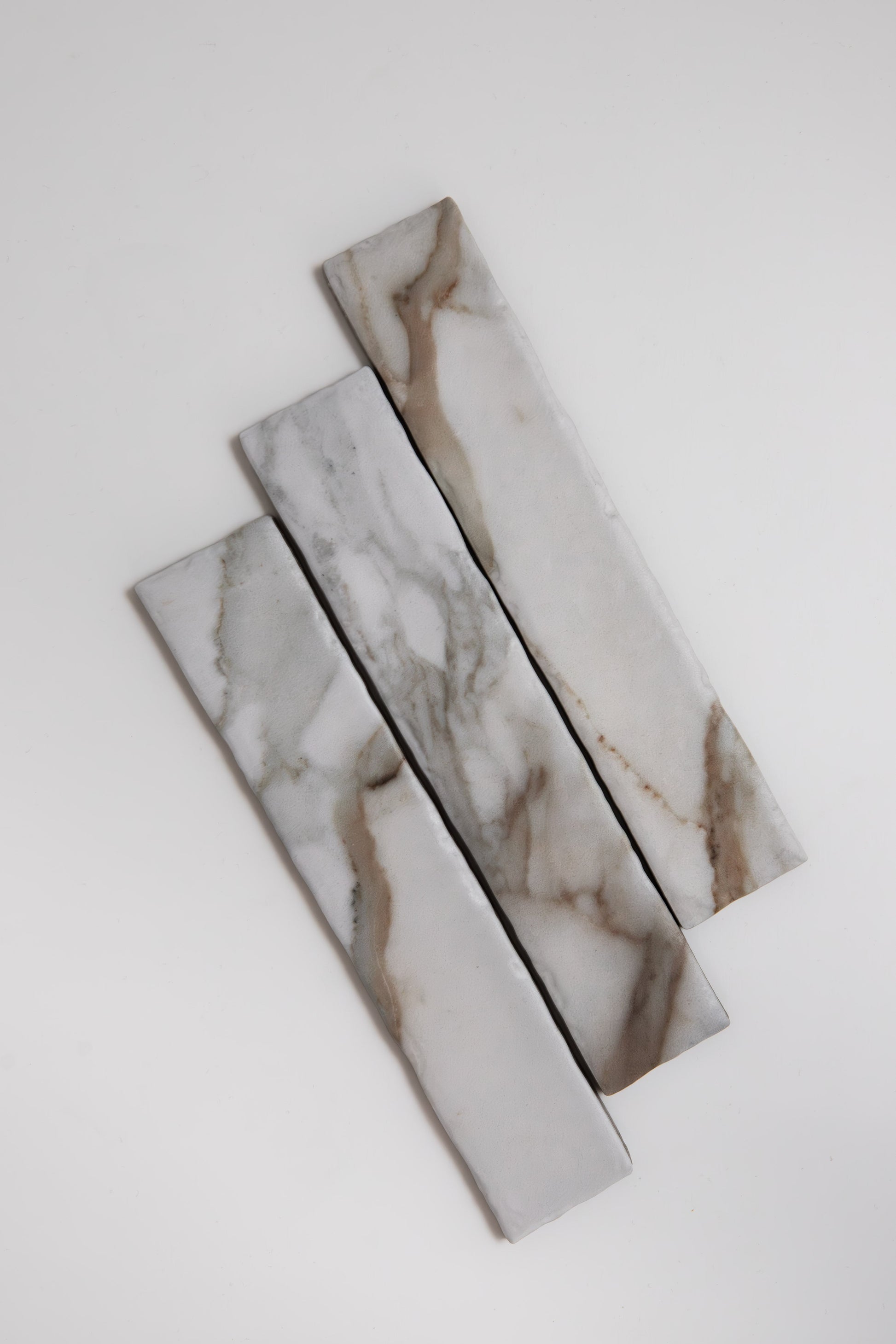Three Macchia Vecchia marble samples from Tosca, with gray and brown veining, set diagonally on a white background.