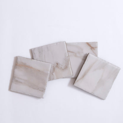 Four Tosca Macchia Vecchia marble sample tiles with light gray and beige veining displayed on a white background.