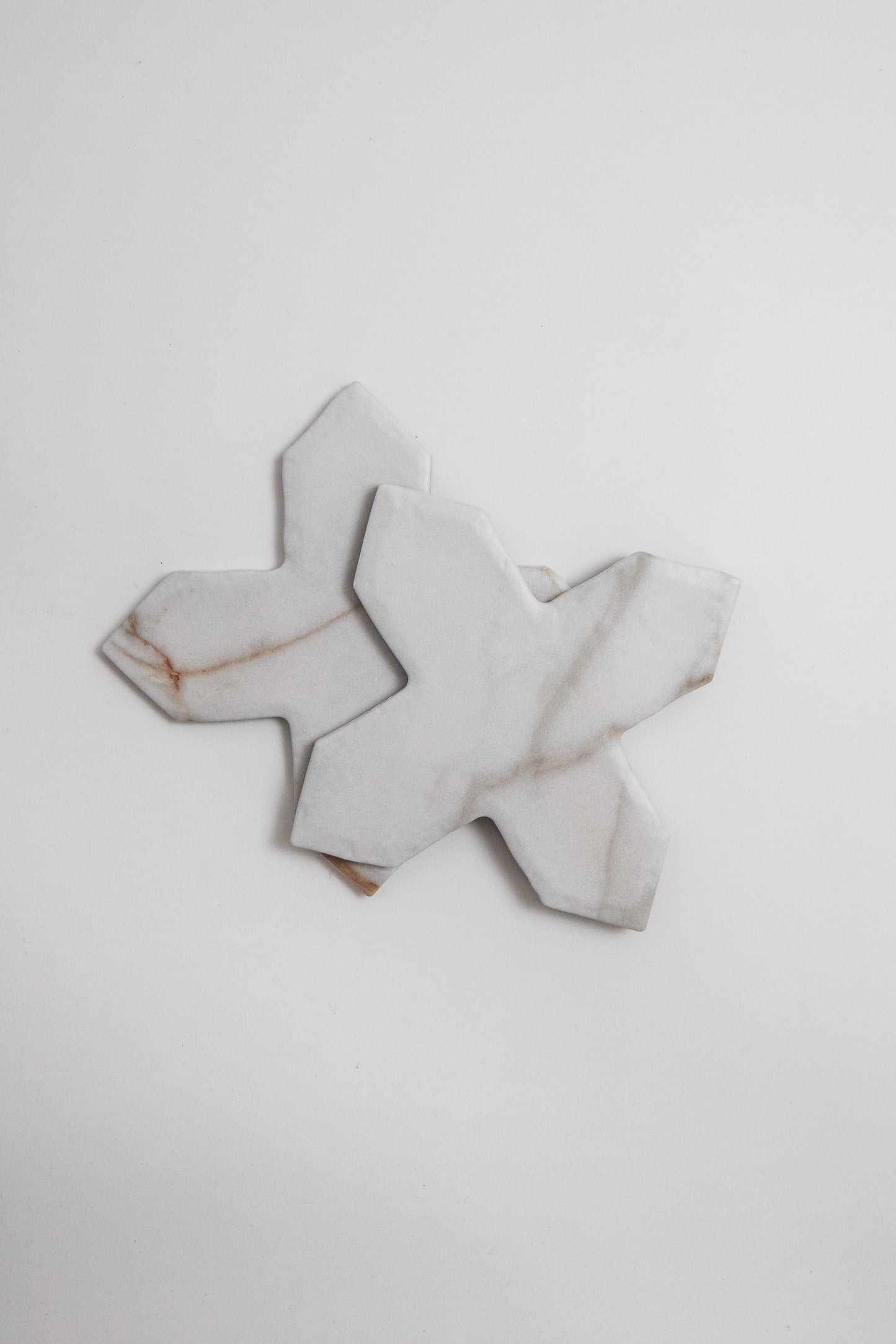 Two Tosca Macchia Vecchia Extra marble samples, X-shaped with gray and brown veining, on a white surface.
