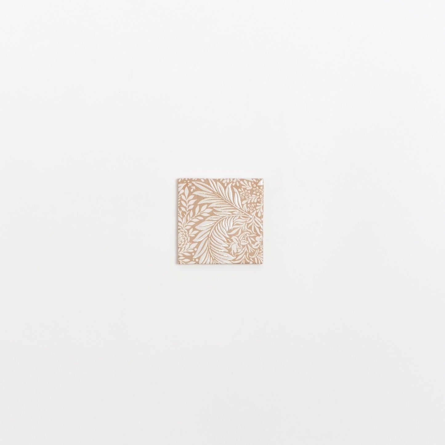 The Maisie Deco sample by Cottage Ivy is a small square tile with an intricate white floral pattern on beige.