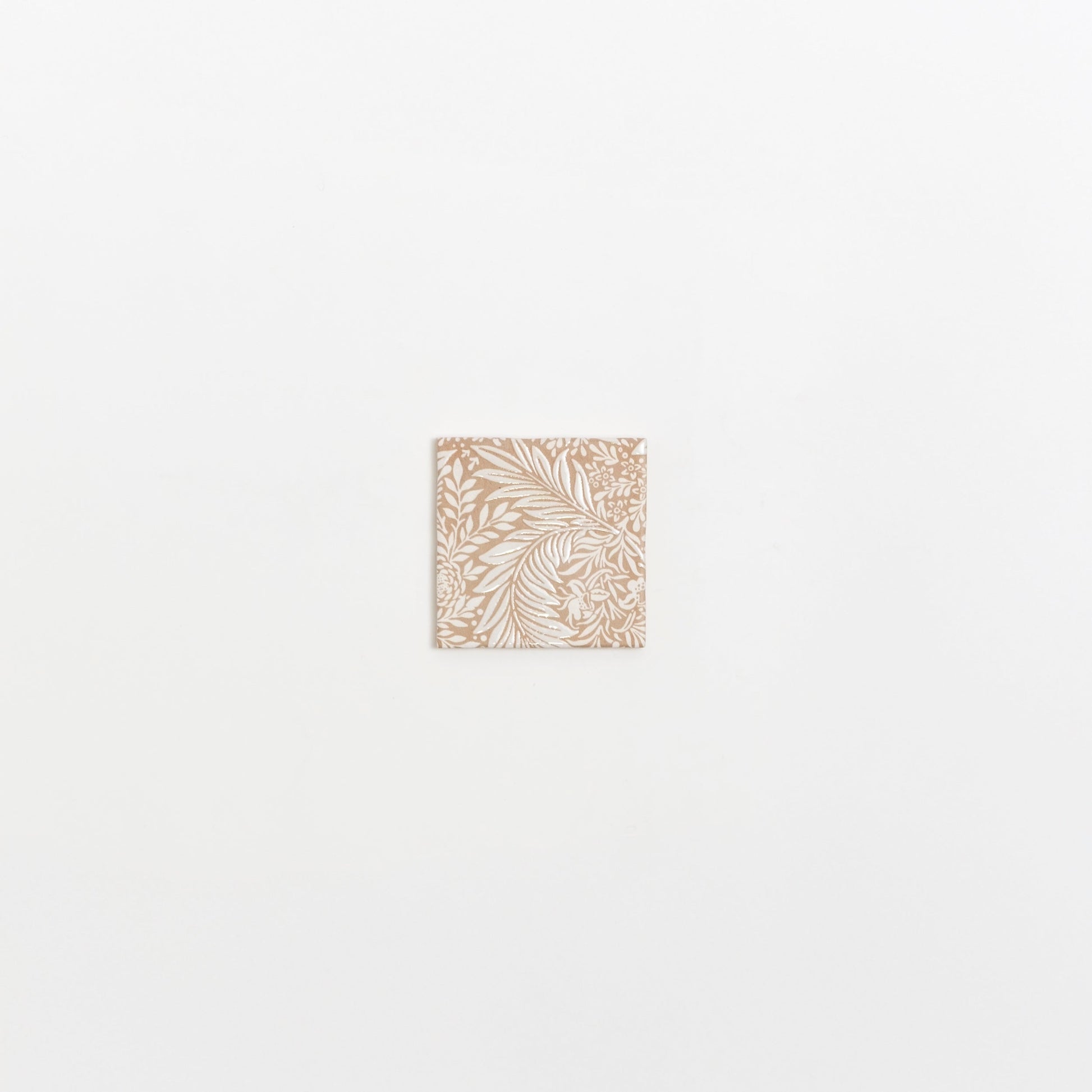 The Maisie Deco sample by Cottage Ivy is a small square tile with an intricate white floral pattern on beige.