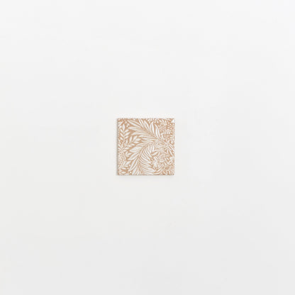 The Maisie Deco sample by Cottage Ivy is a small square tile with an intricate white floral pattern on beige.