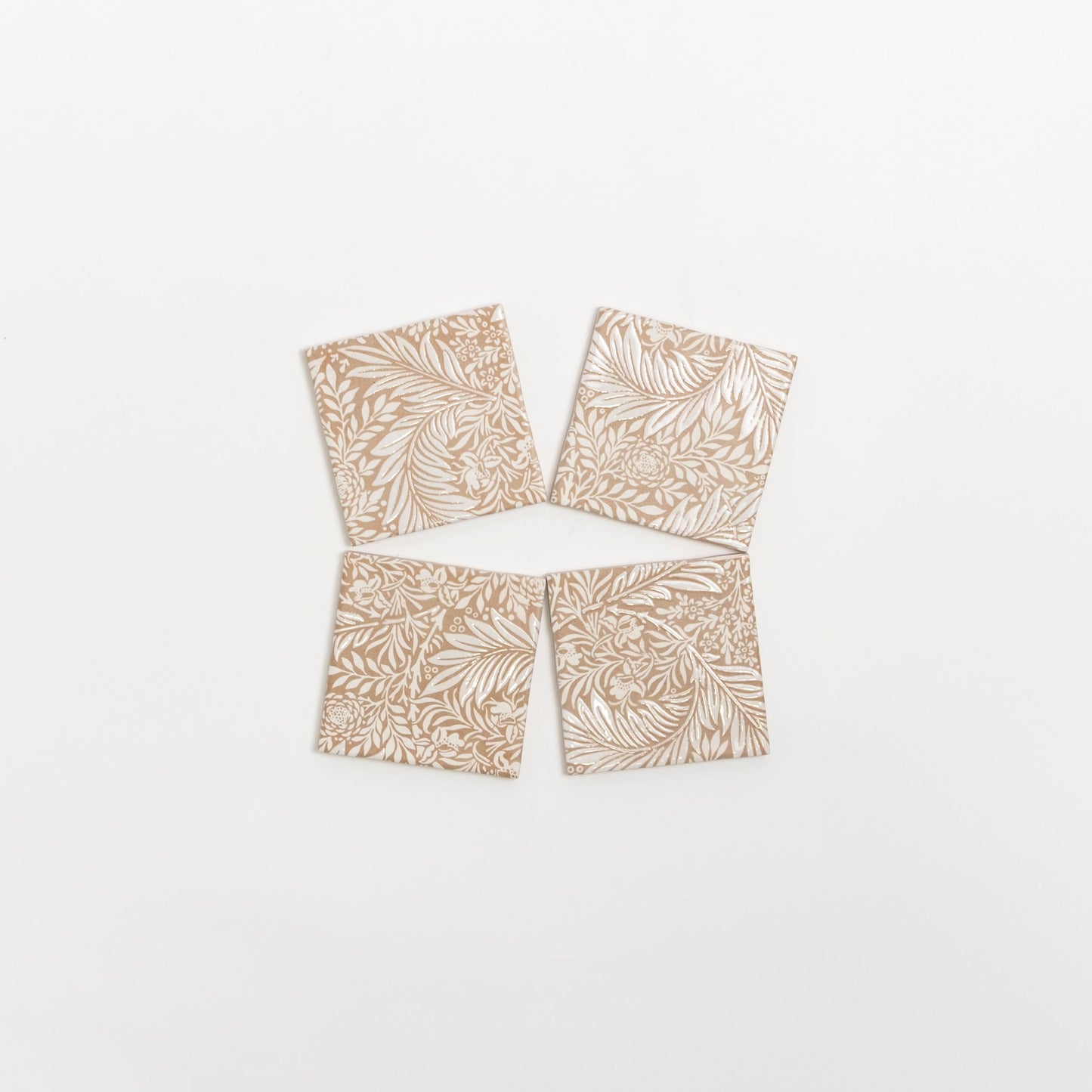 Four Maisie Deco tile samples by Cottage Ivy, beige with white leaf and floral patterns, arranged in a loose diamond shape.