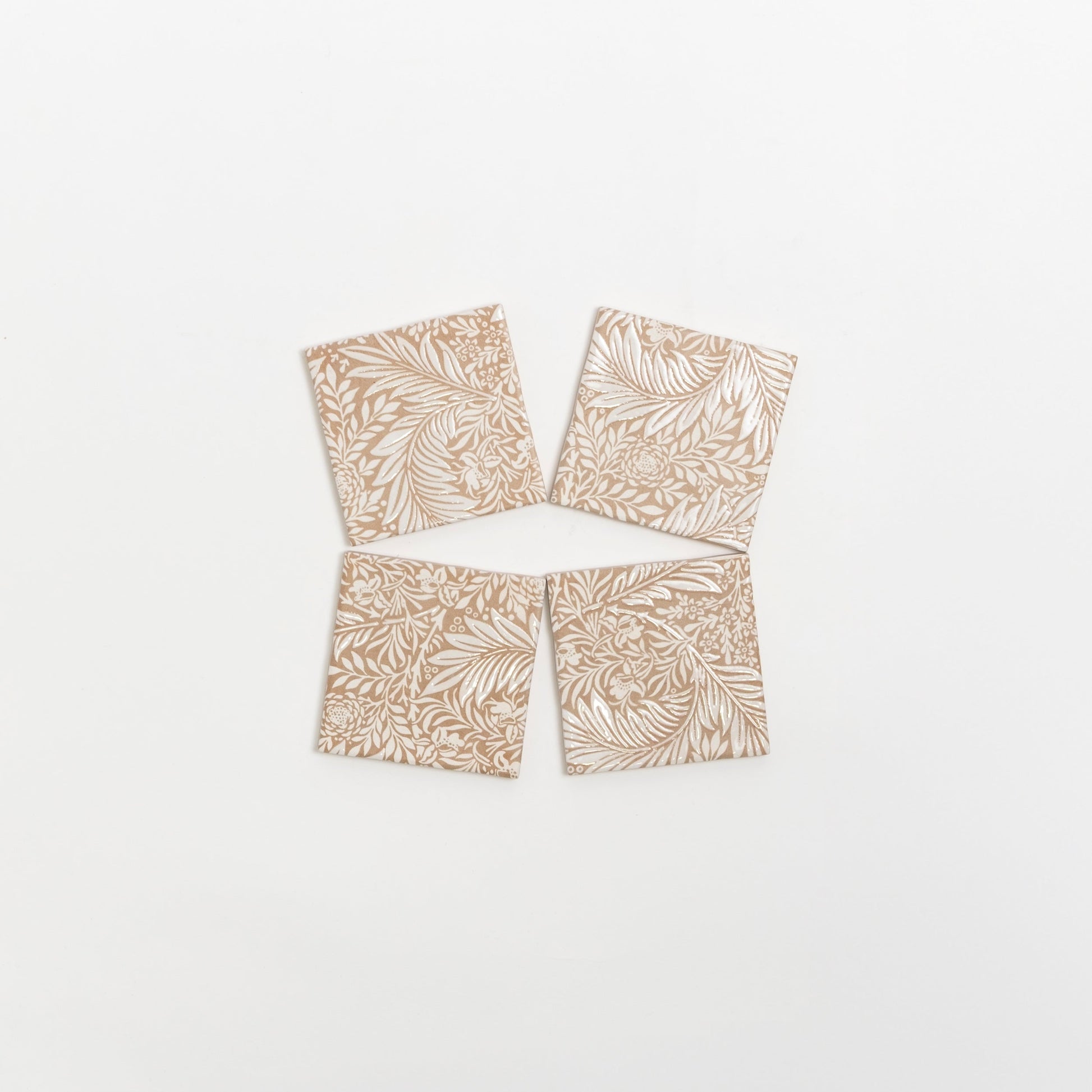 Four Maisie Deco tile samples by Cottage Ivy, beige with white leaf and floral patterns, arranged in a loose diamond shape.