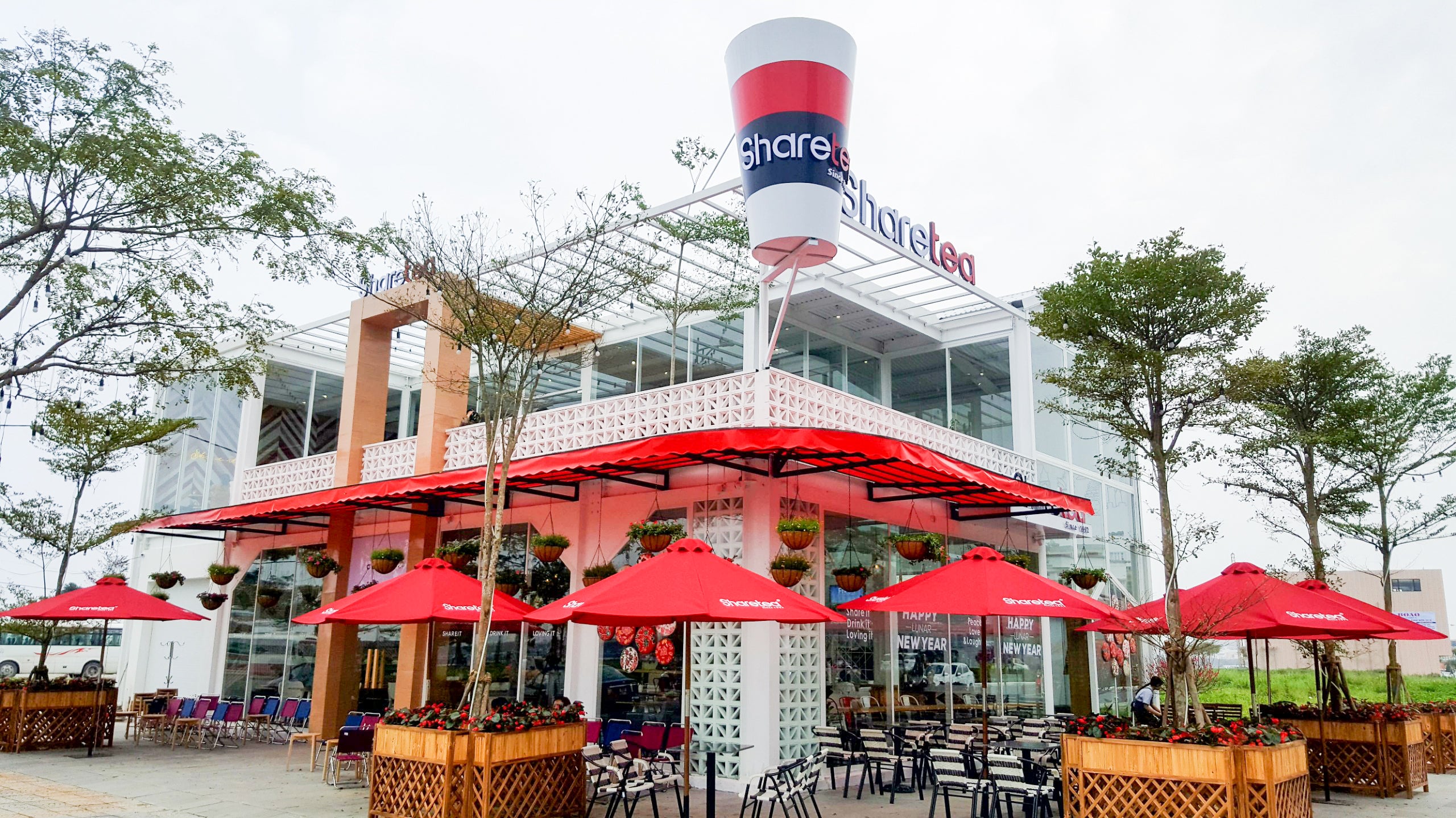Kaui by New York Cement Tile adds mid-century style to a modern café with outdoor seating and red umbrellas among trees.