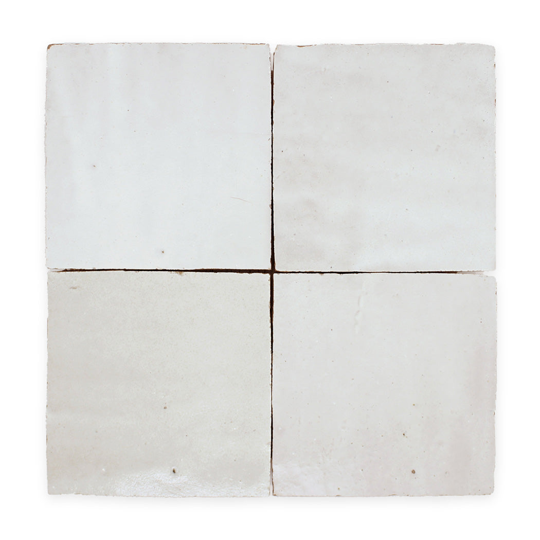 Four square, white ceramic tiles arranged in a 2x2 grid, each with slight variations in texture and sheen.
