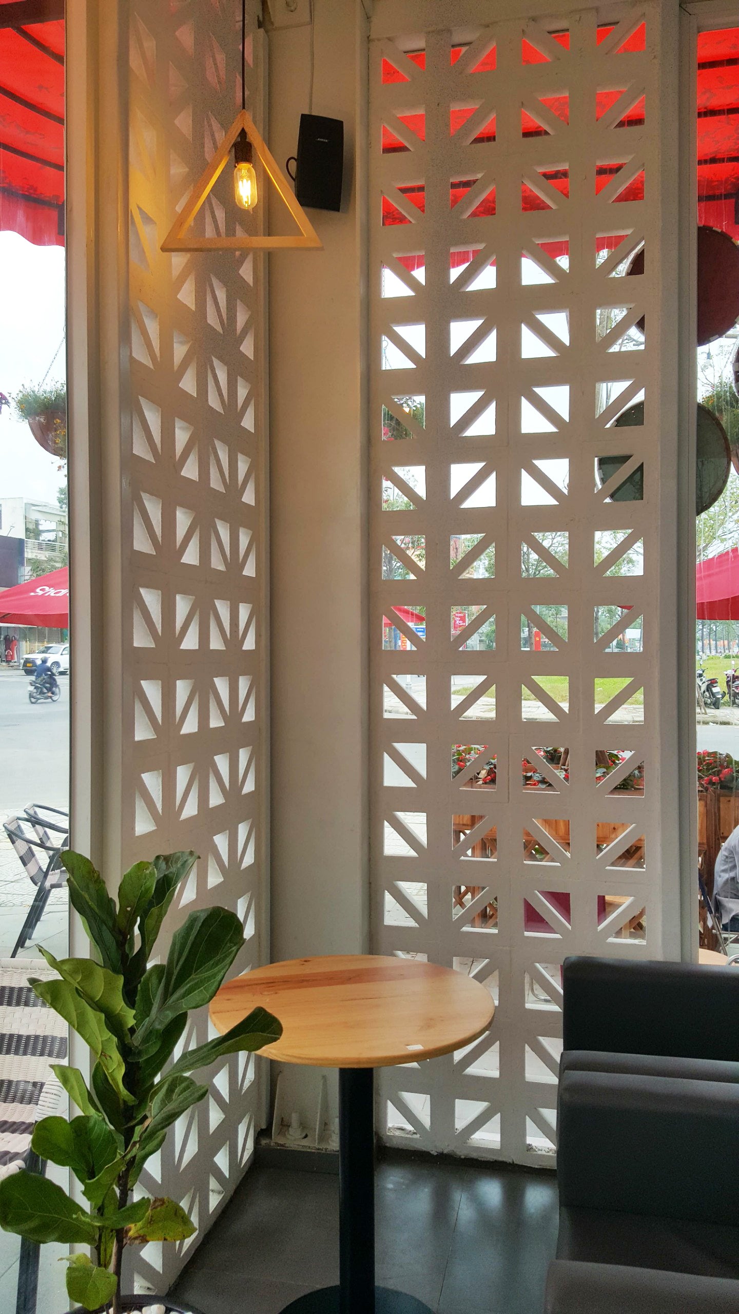 A Kaui table by New York Cement Tile sits by a plant near a partition and triangle light in a cozy café.