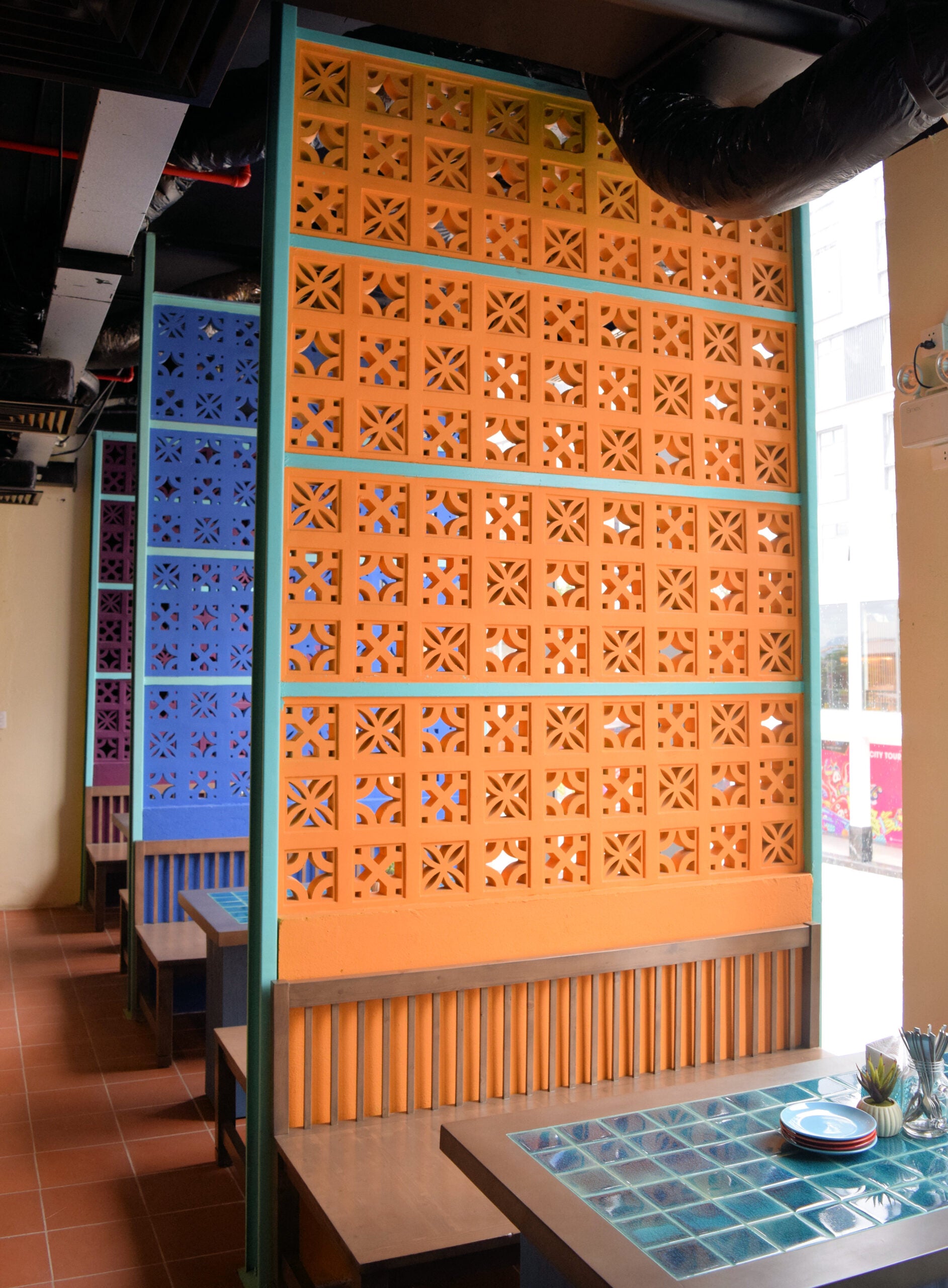 Sam booth seating by New York Cement Tile beside geometric cutout partitions in a brightly lit restaurant.