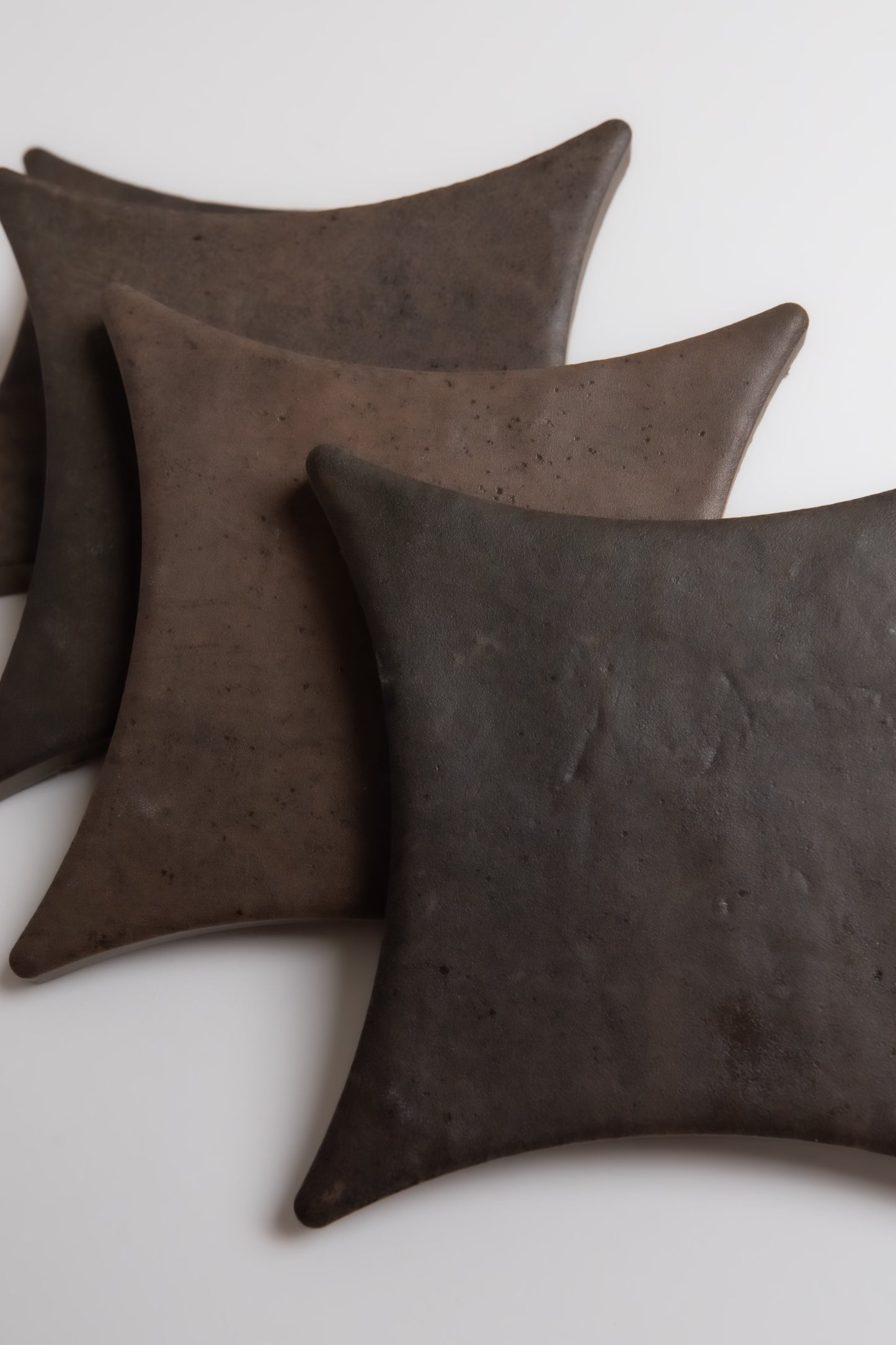 Three dark Ocre, Extra Sample leather coasters by Finca with curved edges overlap on a white surface.