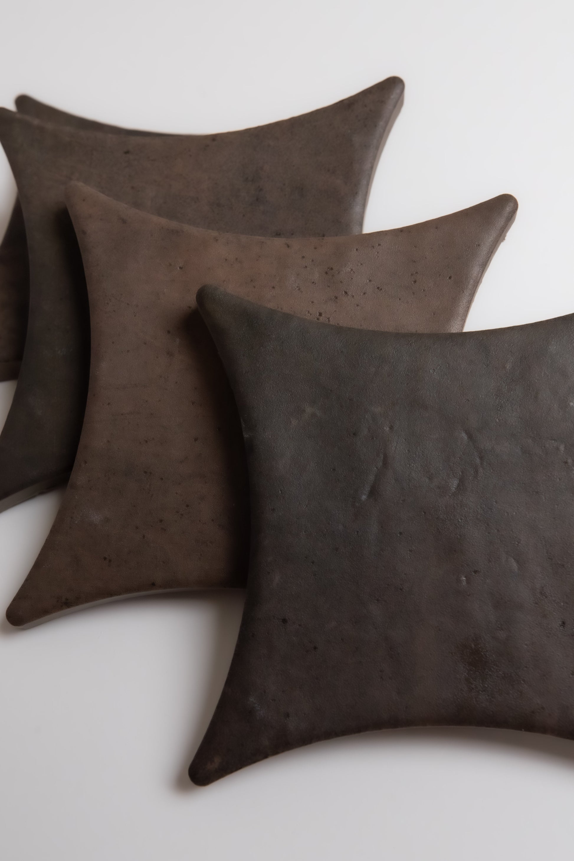 Three dark Ocre, Extra Sample leather coasters by Finca with curved edges overlap on a white surface.
