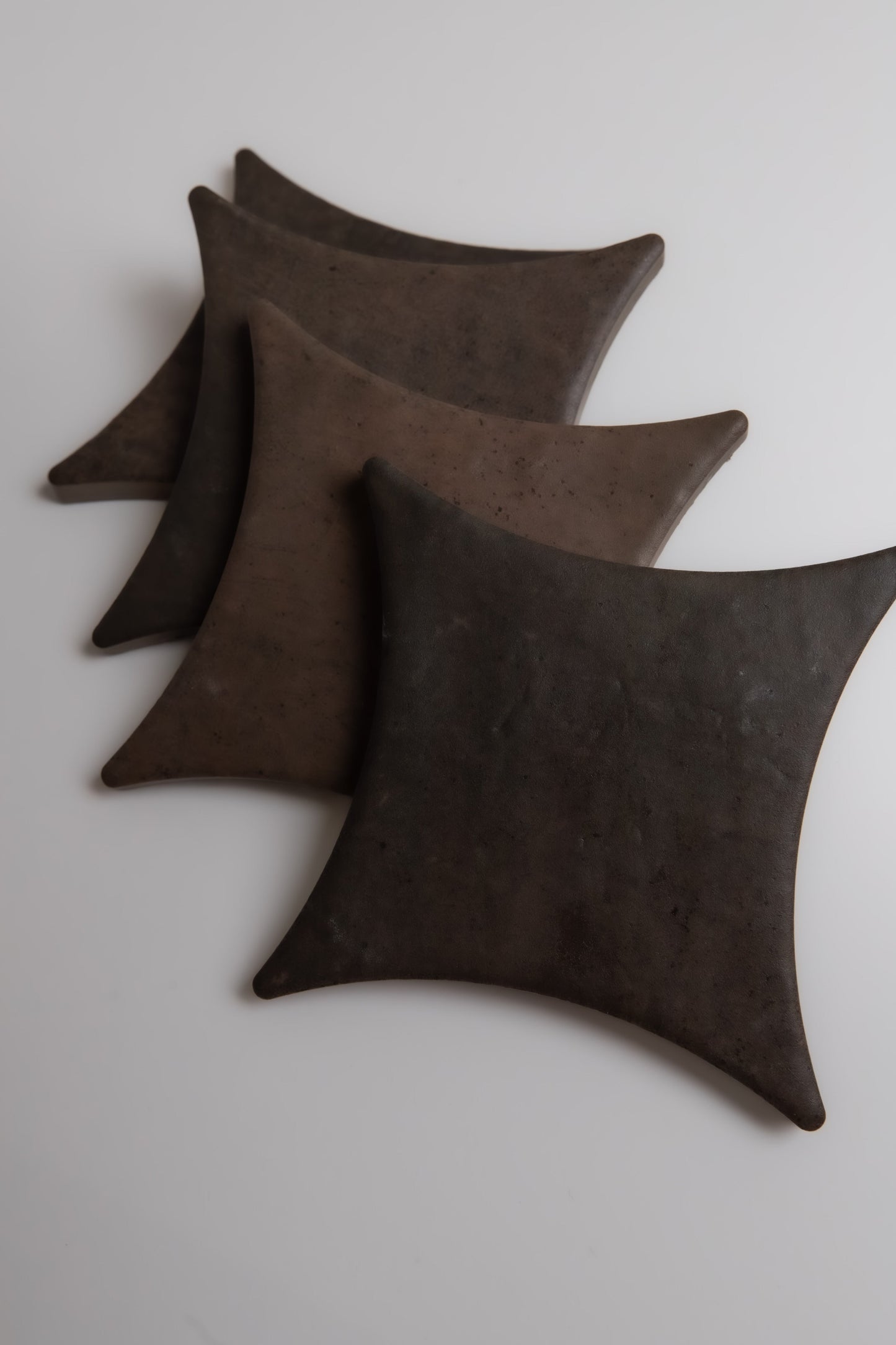 Three dark Ocre, Extra Sample plates by Finca, square with rounded edges, stacked diagonally on a white surface.