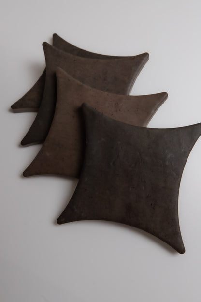 Three dark Ocre, Extra Sample plates by Finca, square with rounded edges, stacked diagonally on a white surface.