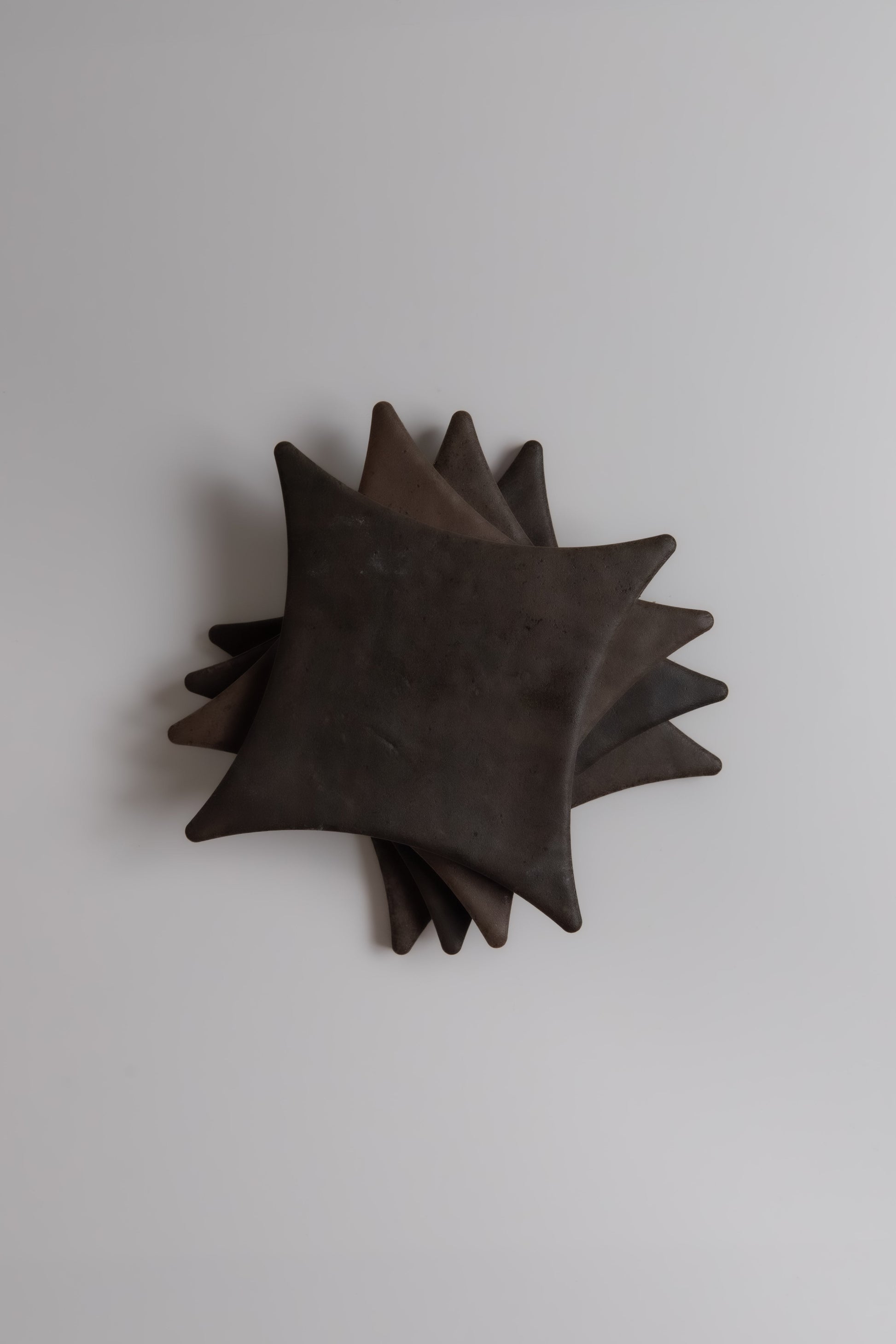 Five overlapping, dark square Finca Ocre Extra Sample ceramic plates with rounded edges on a light gray surface.