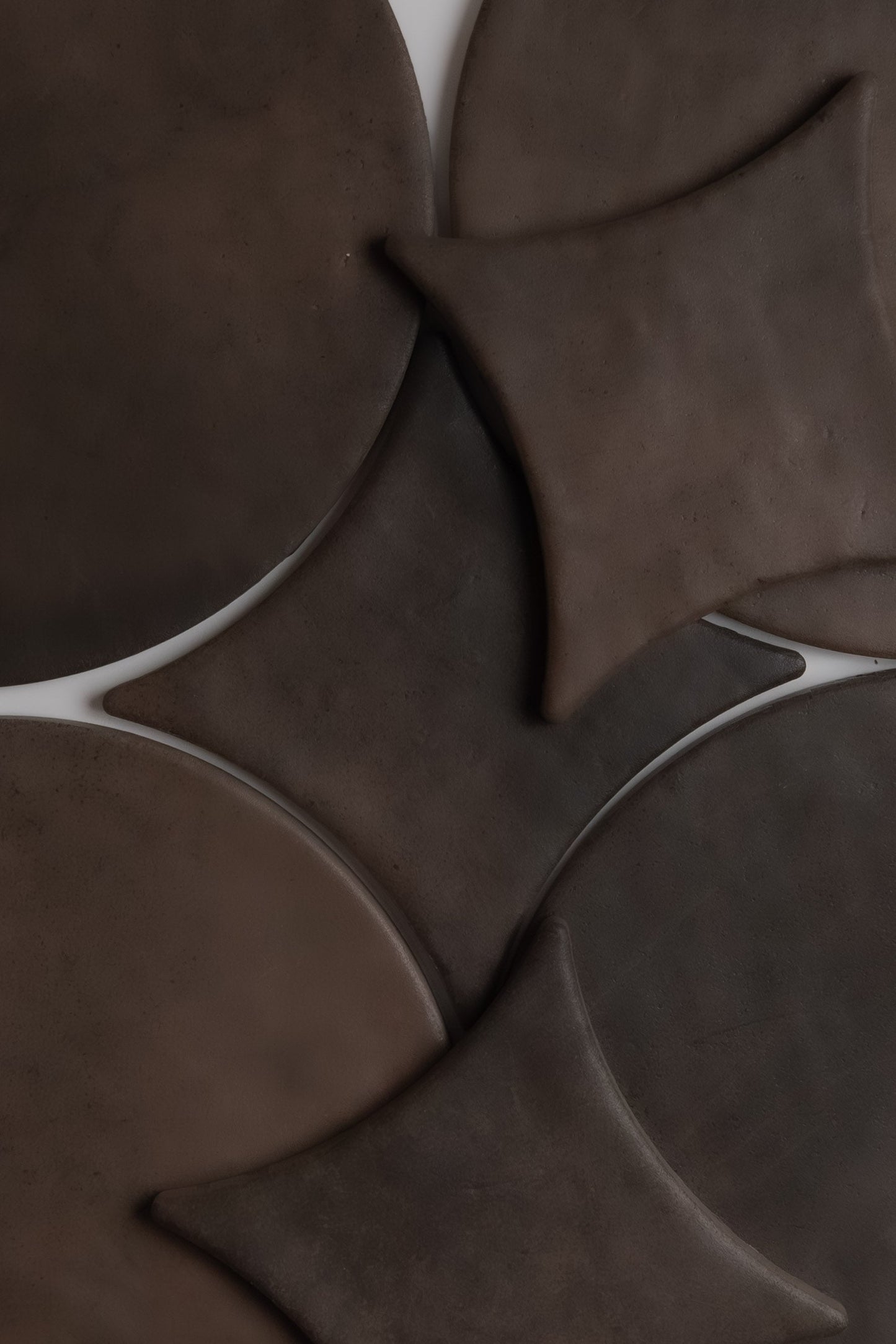 Finca Ocre Extra Sample features dark brown, overlapping round and diamond ceramic tiles in an abstract geometric pattern.
