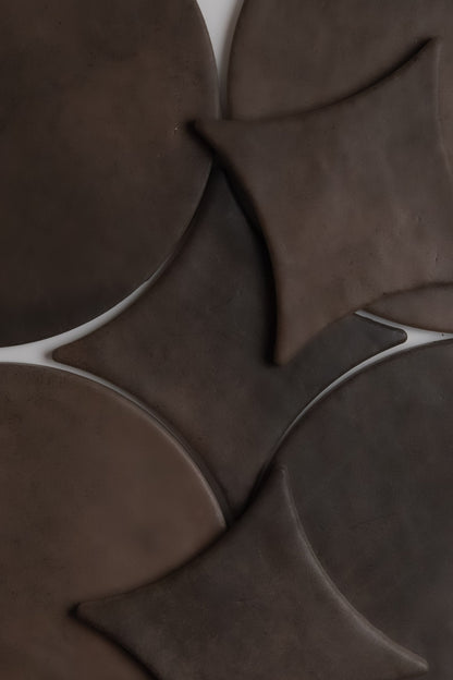 Finca Ocre Extra Sample features dark brown, overlapping round and diamond ceramic tiles in an abstract geometric pattern.