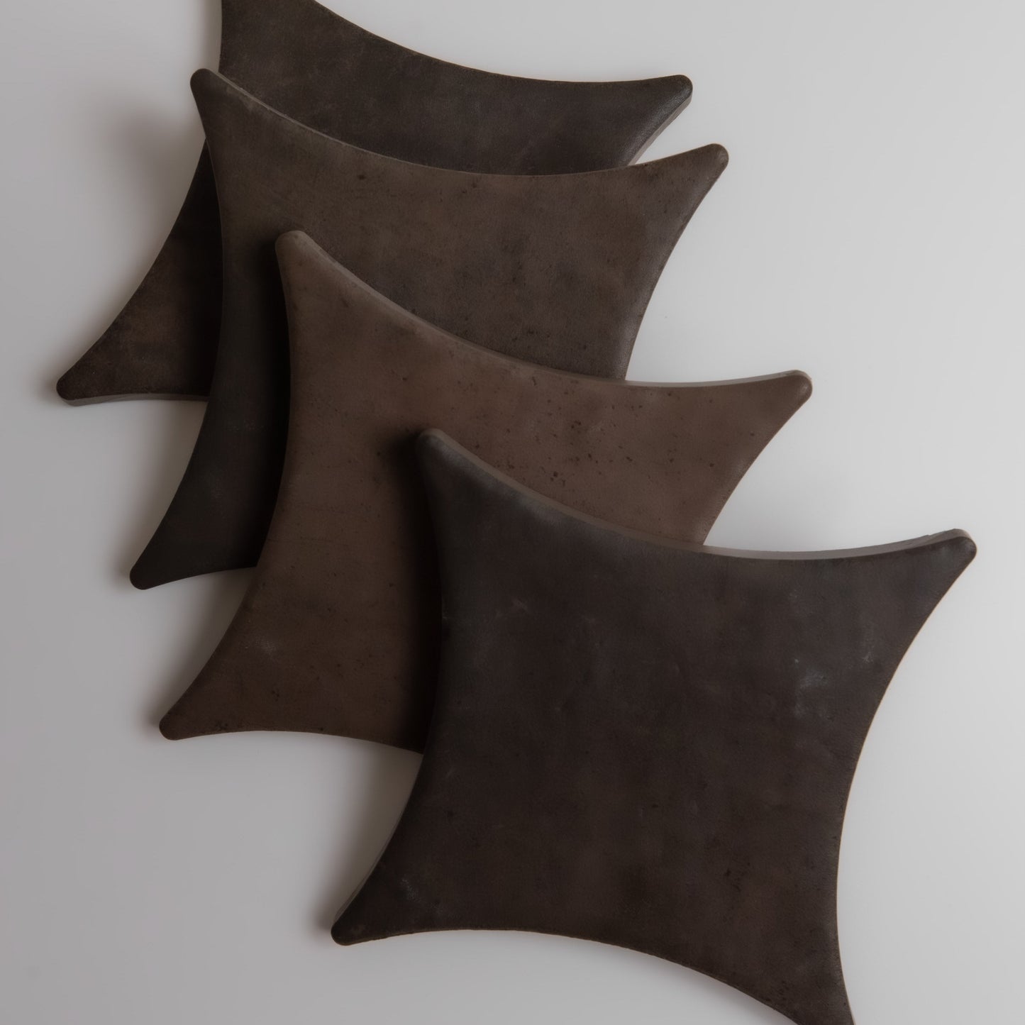 Four "Ocre, Extra Sample" star cushions by Finca in dark brown, arranged diagonally on a light surface.