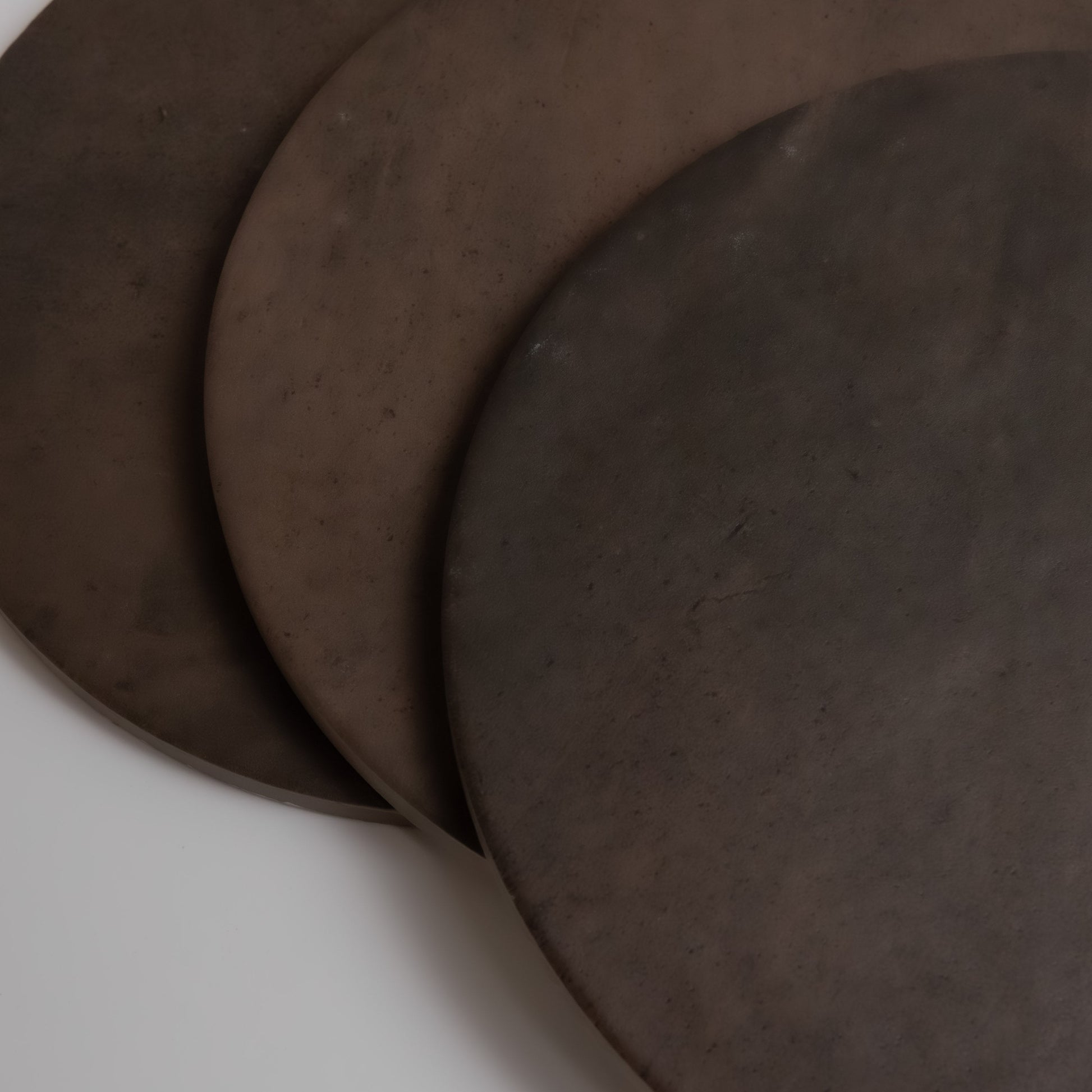 Three overlapping round Finca Ocre, Extra Sample dark brown ceramic plates on a white surface.